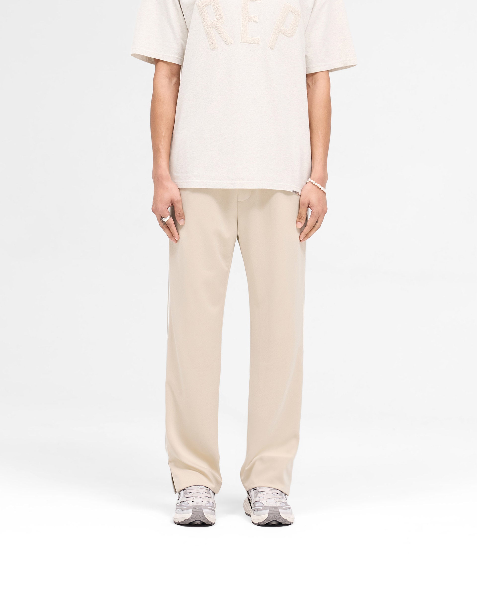 Man wearing tailored stone pants on a plain white background | Tailored Track Pant in Stone | Pants with elasticated waistband and zip detail | SS25 Pants | Represent Clo