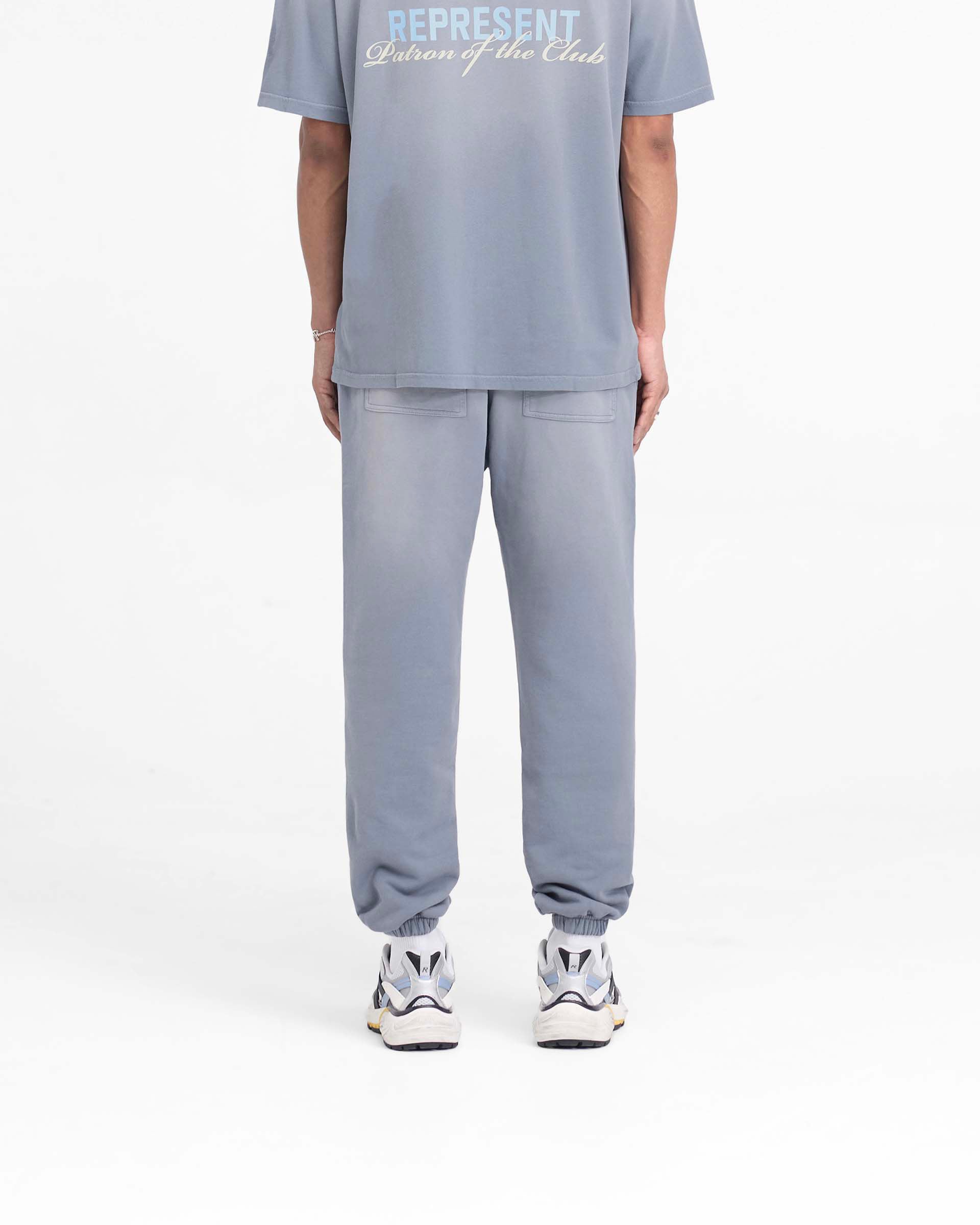 Man wearing grey sweatpants on a plain white background | Patron Of The Club Sweatpant in Washed Grey | Sweatpants with elasticated waistband and cuffs | Patrons Pants | Represent Clo