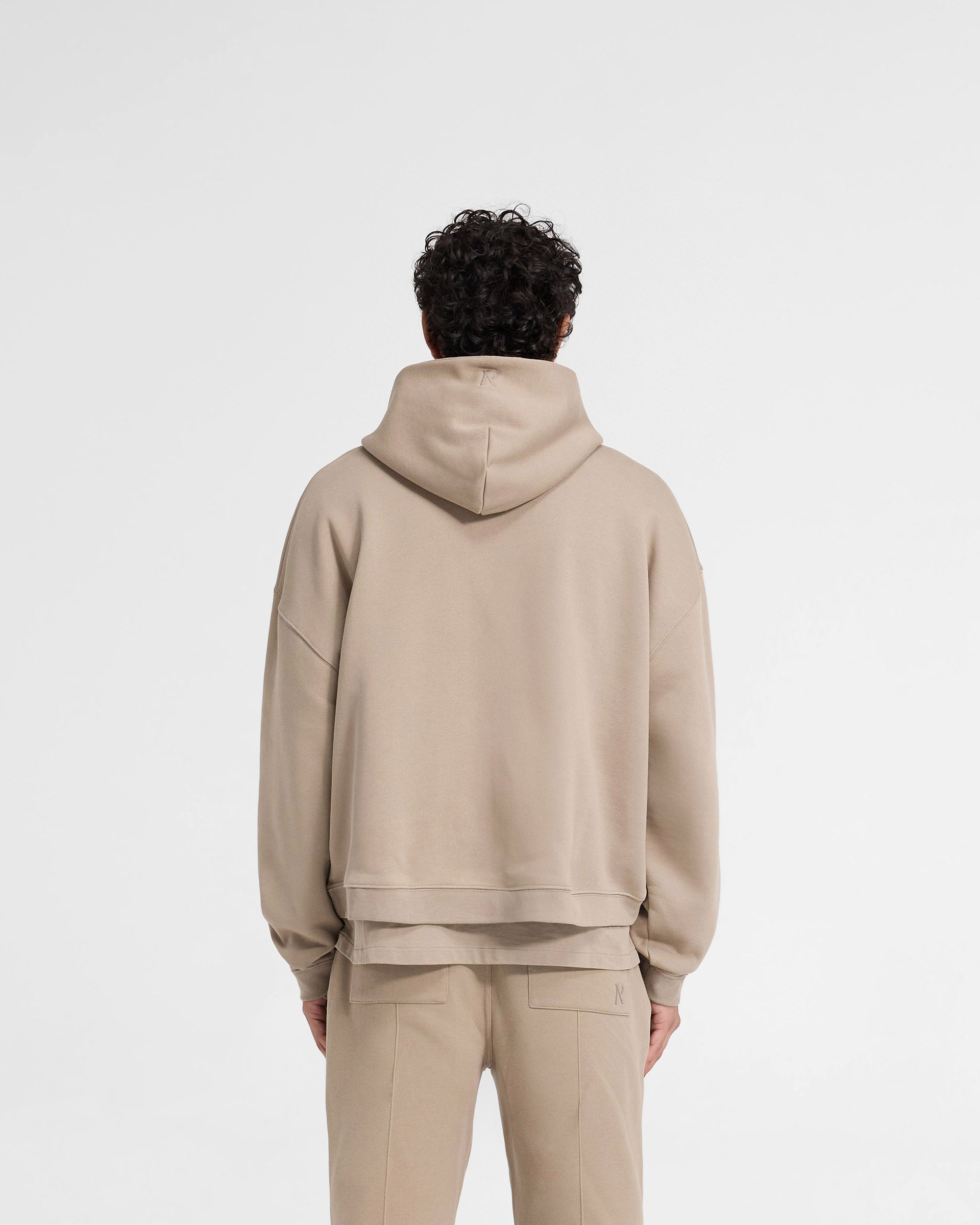 Man wearing an oversized dune hoodie on a plain white background | Initial Boxy Hoodie in Dune | Boxy fit hoodie with cropped body and dropped shoulders | Initial Hoodies | Represent Clo