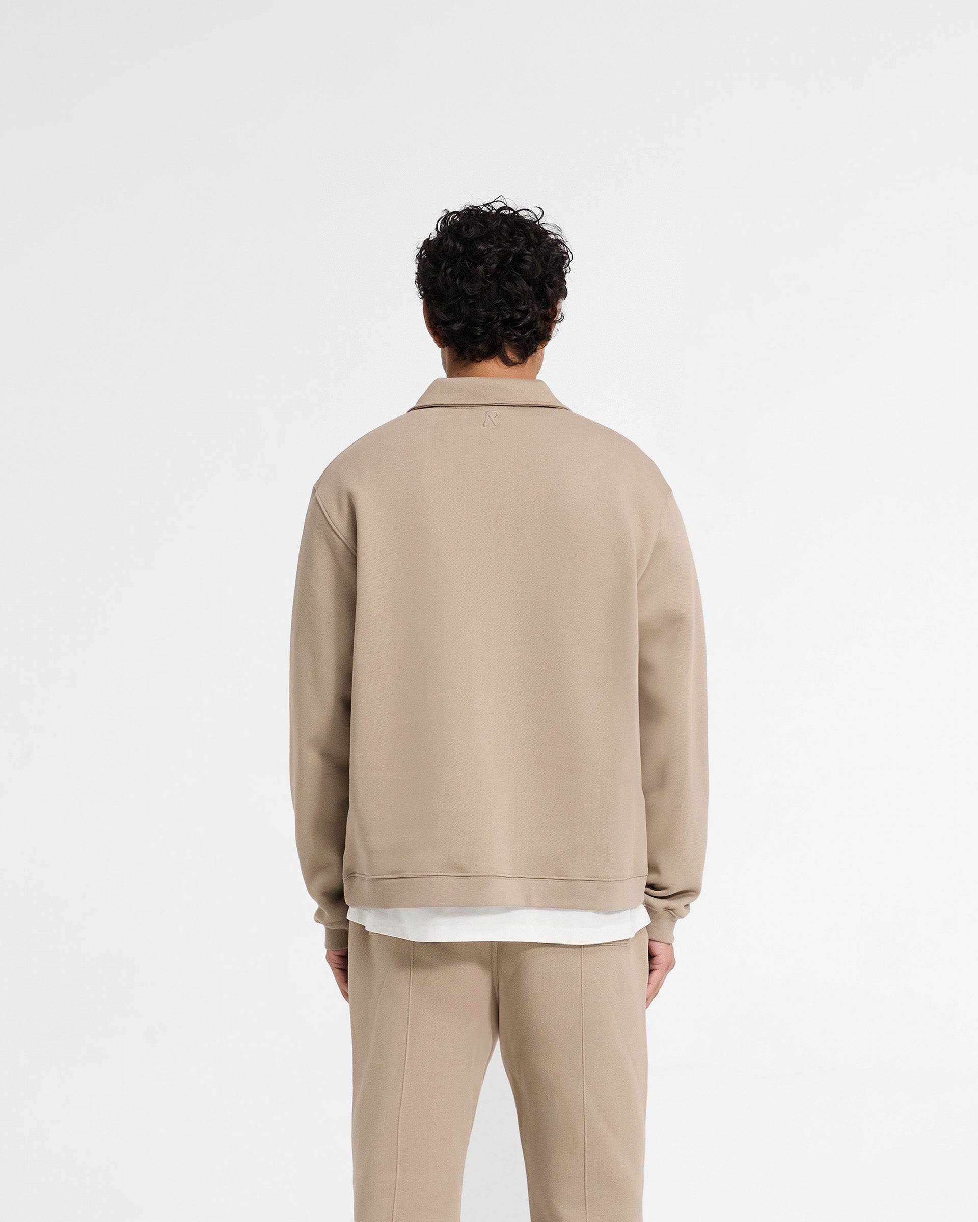 Man wearing a cropped beige quarter zip sweater on a plain white background | Initial Boxy Quarter Zip in Dune | Oversized boxy fit with RiRi zip | Initial Sweaters | Represent Clo