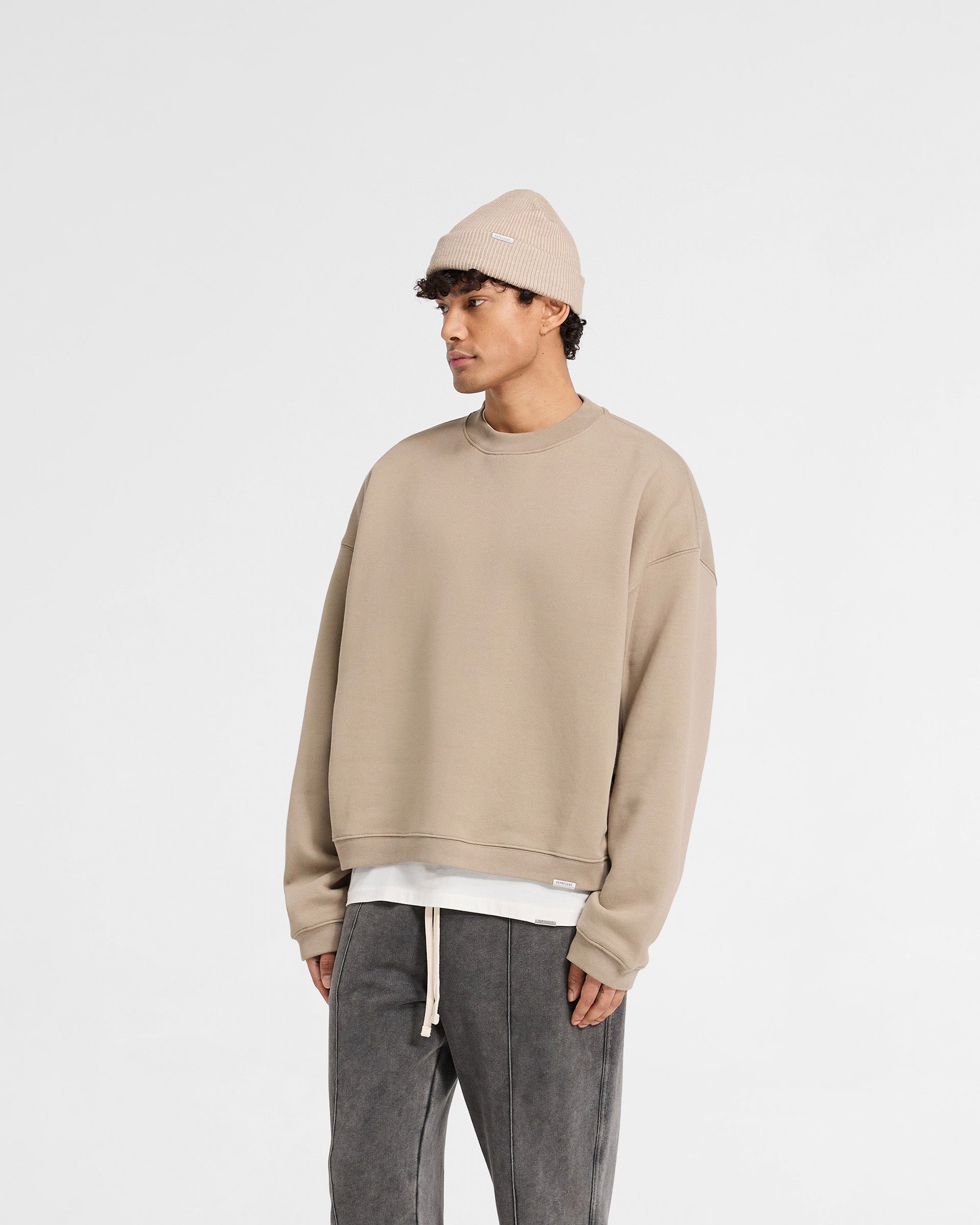 Back product image of a mens beige sweater on a plain white background | Initial Boxy Sweater in Dune | Boxy fit sweater with embroidered initial and metal bar | Initial Sweaters | Represent Clo