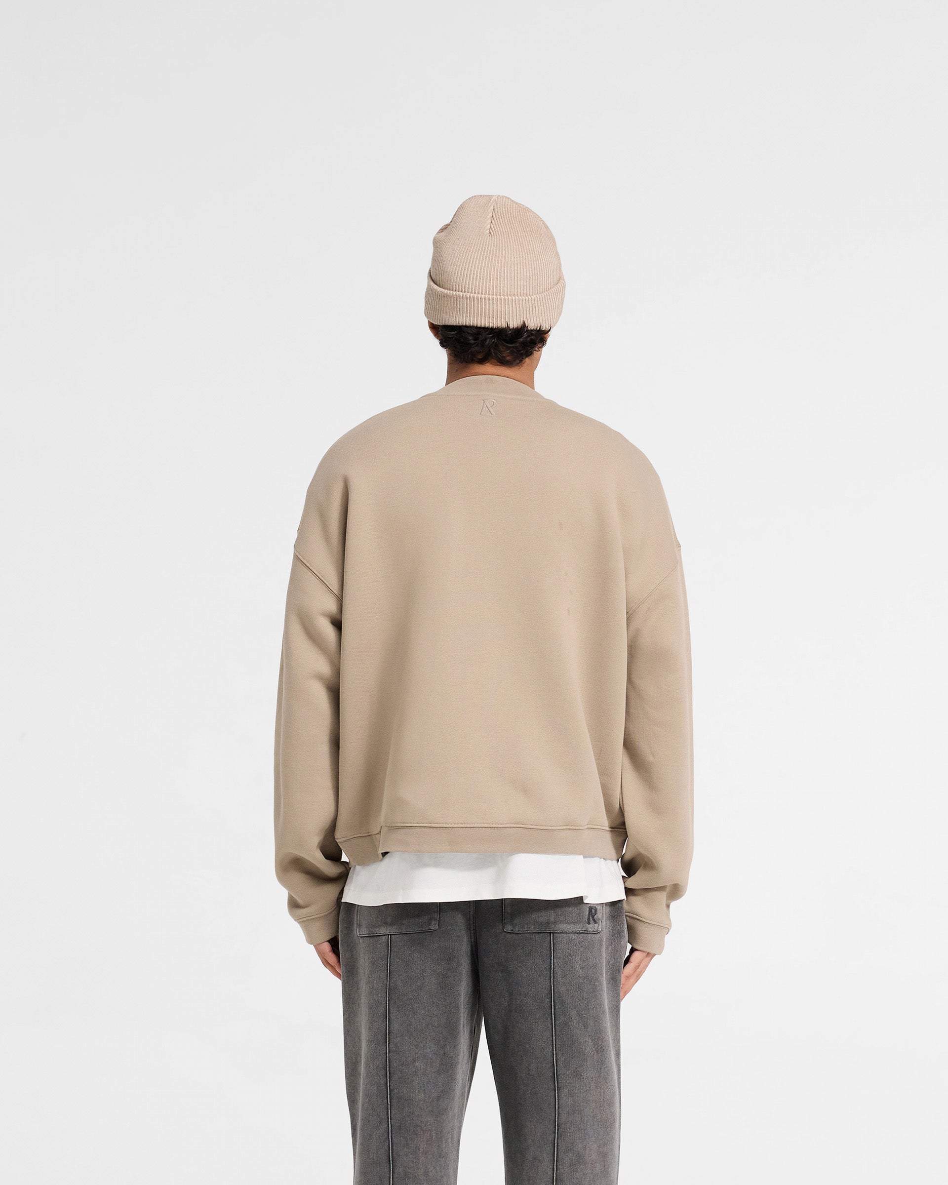 Man wearing an oversized beige sweater on a plain white background | Initial Boxy Sweater in Dune | Boxy fit sweater with super cropped body | Initial Sweaters | Represent Clo