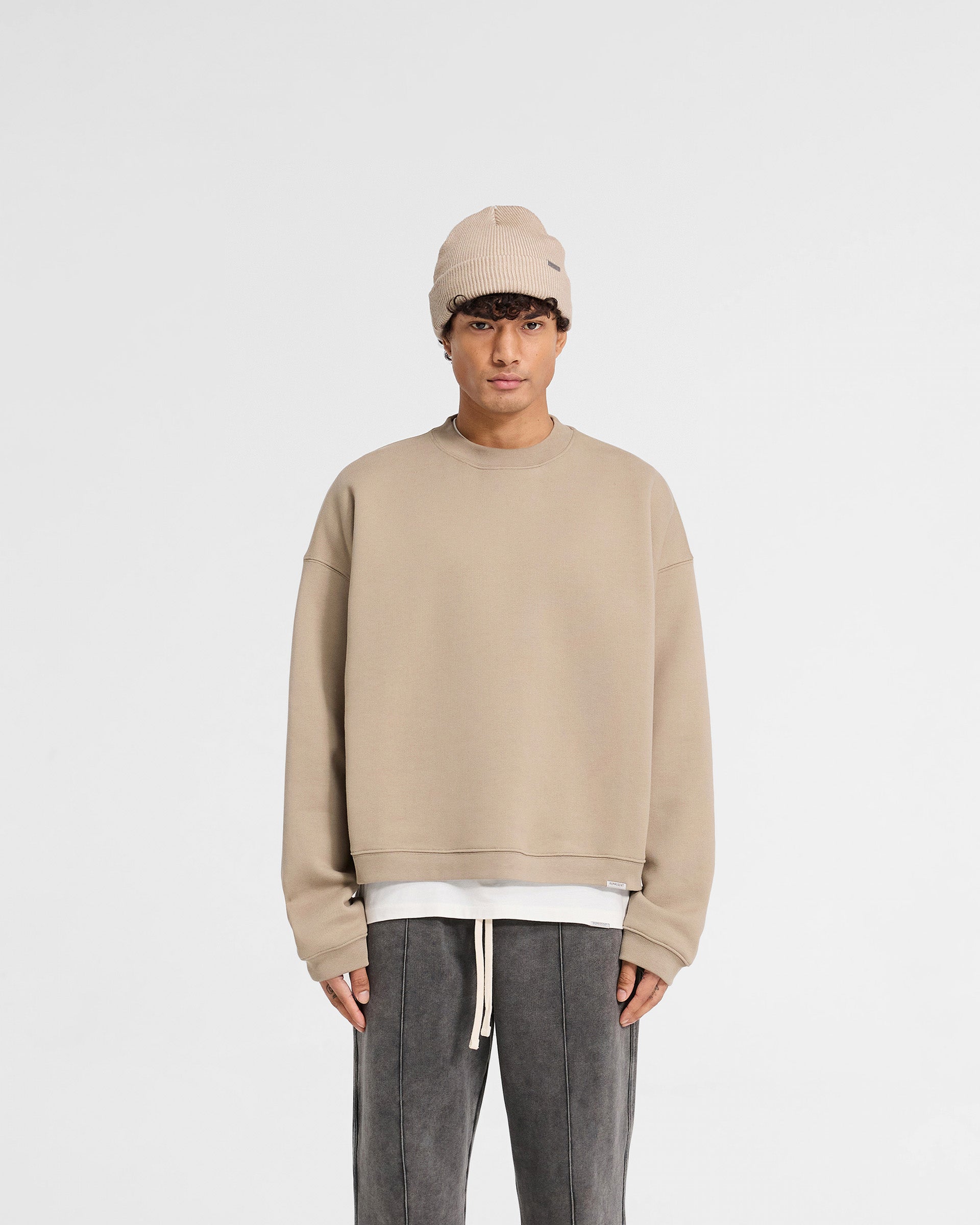 Man wearing a beige oversized sweater on a plain white background | Initial Boxy Sweater in Dune | Boxy fit sweater with dropped shoulders | Initial Sweaters | Represent Clo