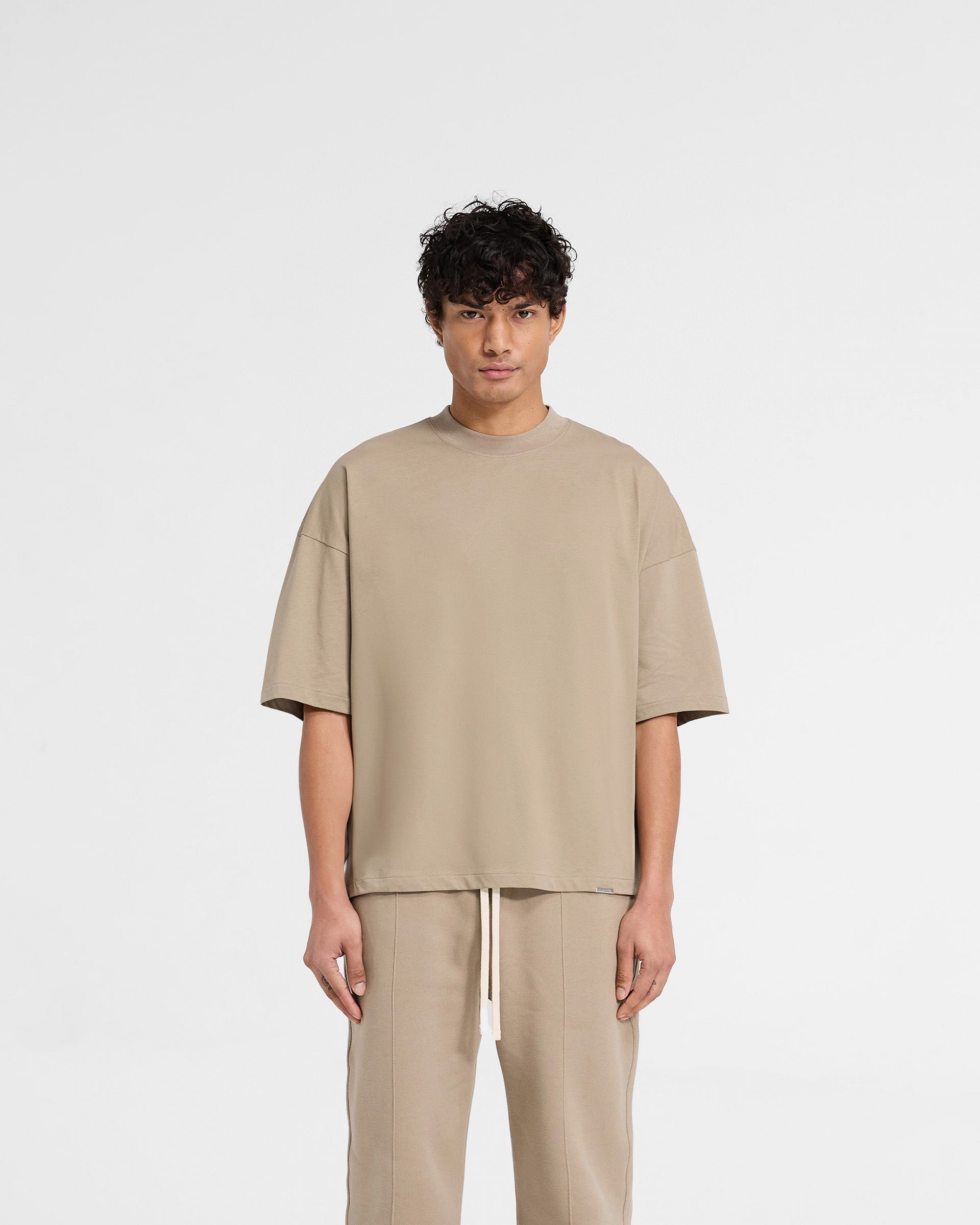Man wearing an oversized dune t-shirt on a plain white background | Initial Boxy T-Shirt in Dune | Oversized and boxy cropped t-shirt in heavy cotton | Initial T-Shirts | Represent Clo