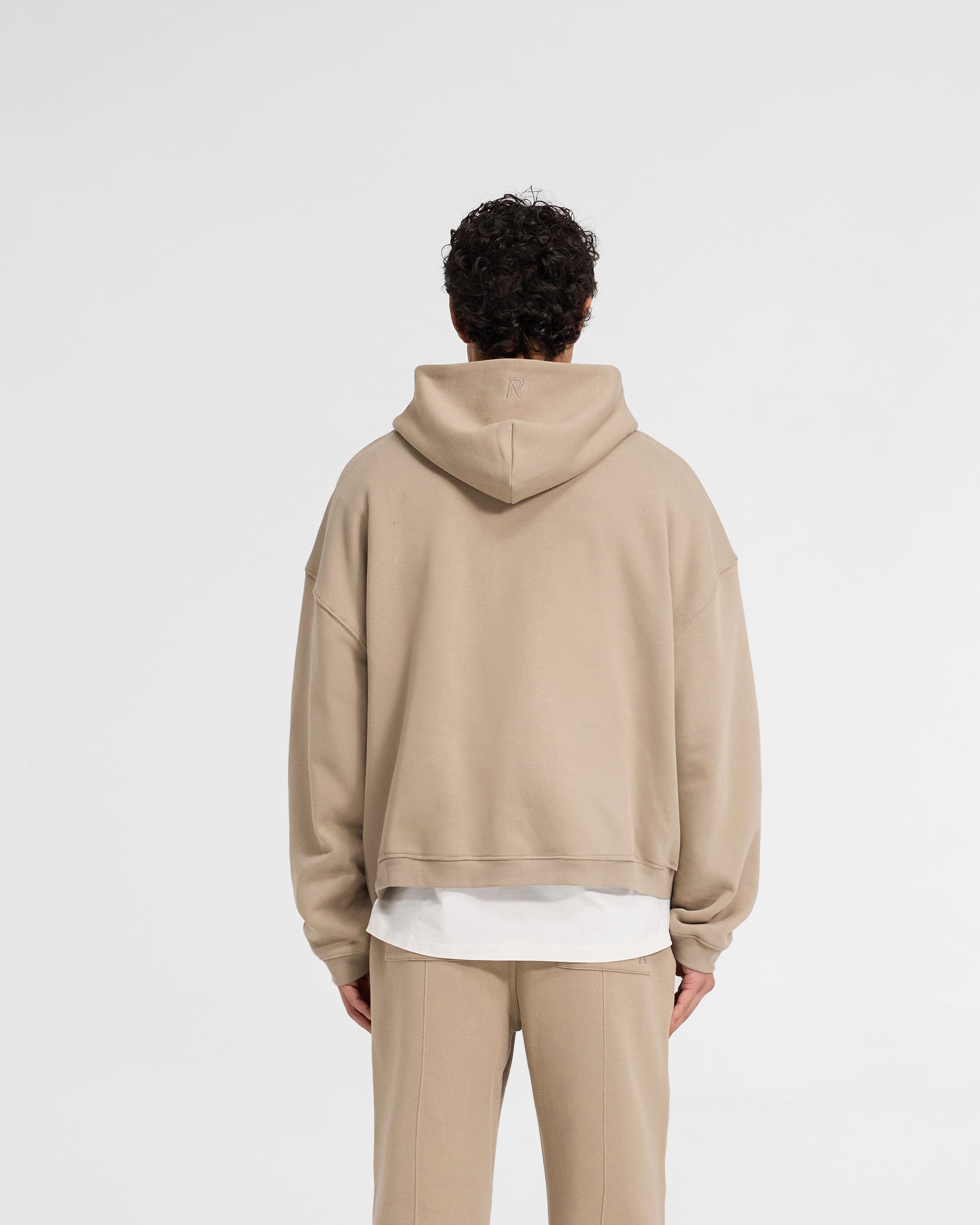 Man wearing an oversized beige hoodie on a plain white background | Initial Boxy Zip Through Hoodie in Dune | Boxy fit hoodie with cropped length and front zip | Initial Hoodies | Represent Clo