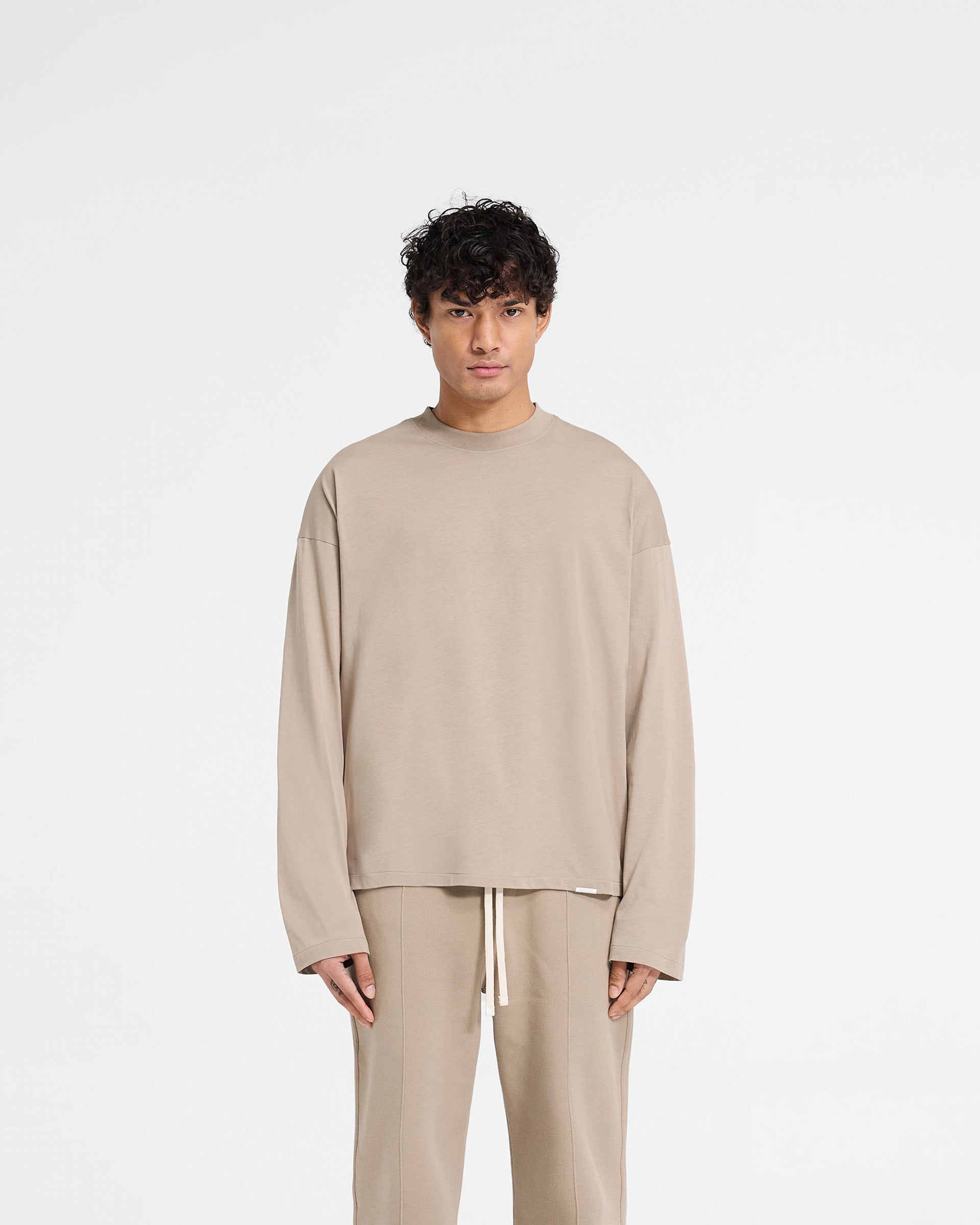 Man wearing a beige t-shirt on a plain white background | Initial Long Sleeve Open Cuff T-Shirt in Dune | Boxy oversized long sleeve t-shirt | Initial T-Shirts | Represent Clo