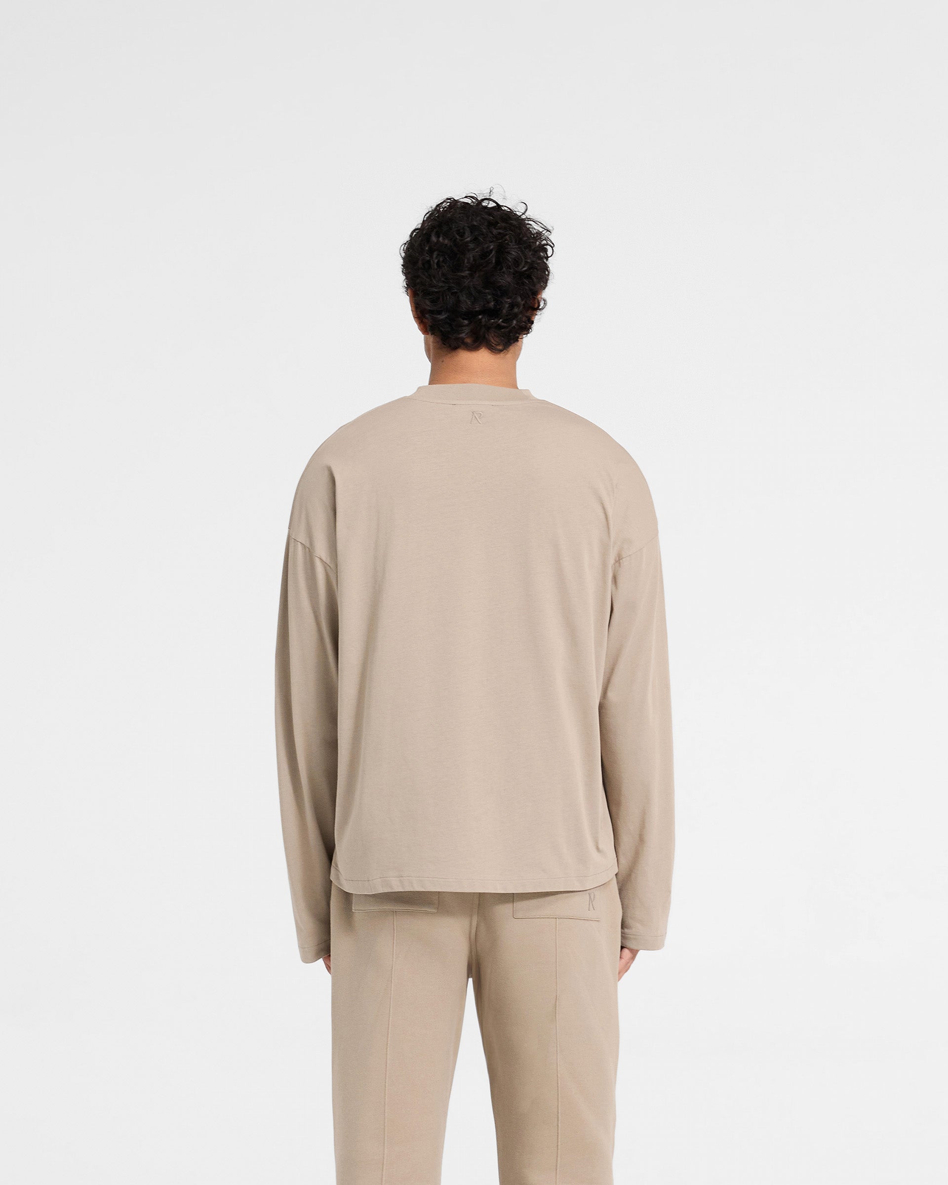 Man wearing an oversized dune long sleeve t-shirt on a plain white background | Initial Long Sleeve Open Cuff T-Shirt in Dune | Boxy fit with open cuffs | Initial T-Shirts | Represent Clo