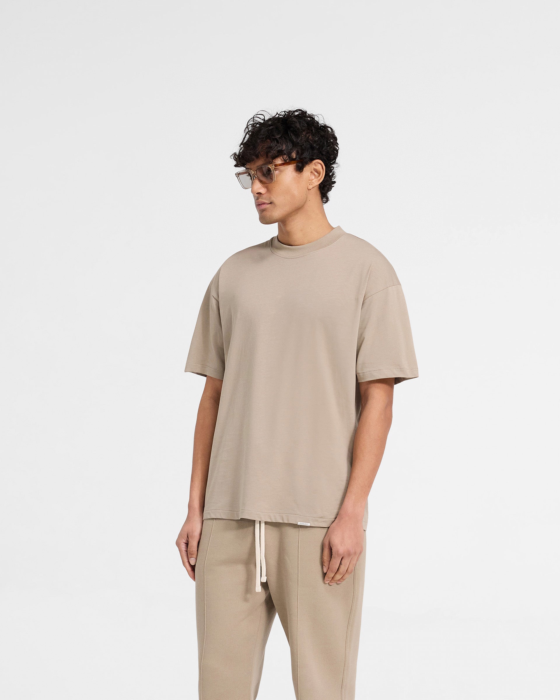 Back product image of a mens beige t-shirt on a plain white background | Initial Oversized T-Shirt in Dune | Oversized fit jersey cotton t-shirt | Initial T-Shirts | Represent Clo
