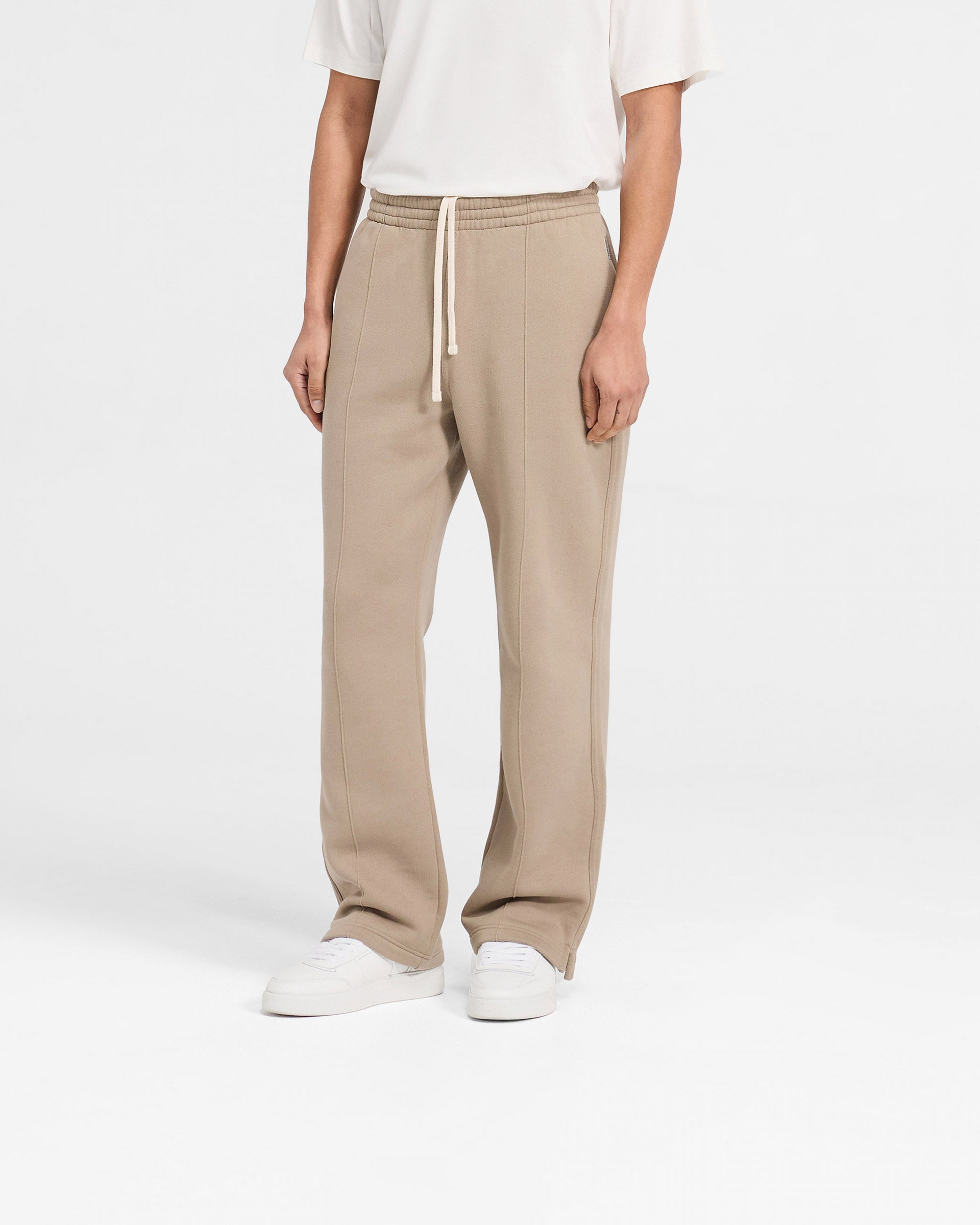 Man wearing beige sweatpants on a plain white background | Initial Sweatpants in Dune | Wide leg style sweatpants with pintuck detail | Initial Pants | Represent Clo