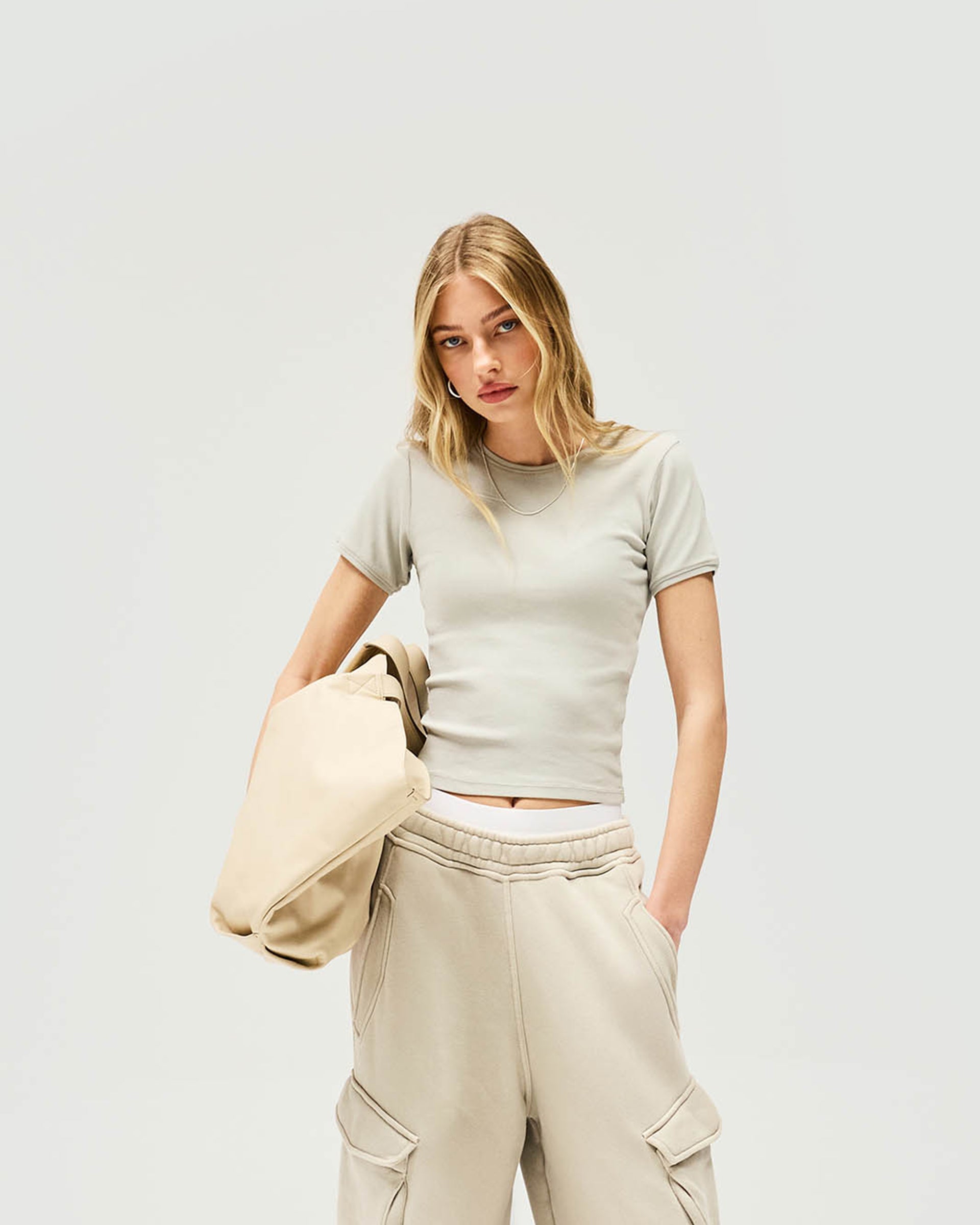 Woman wearing a grey ribbed t-shirt on a plain white background | Initial Rib Baby T-Shirt in Storm | Cropped waist-length fit top | Womens Initial Tops | Represent Clo
