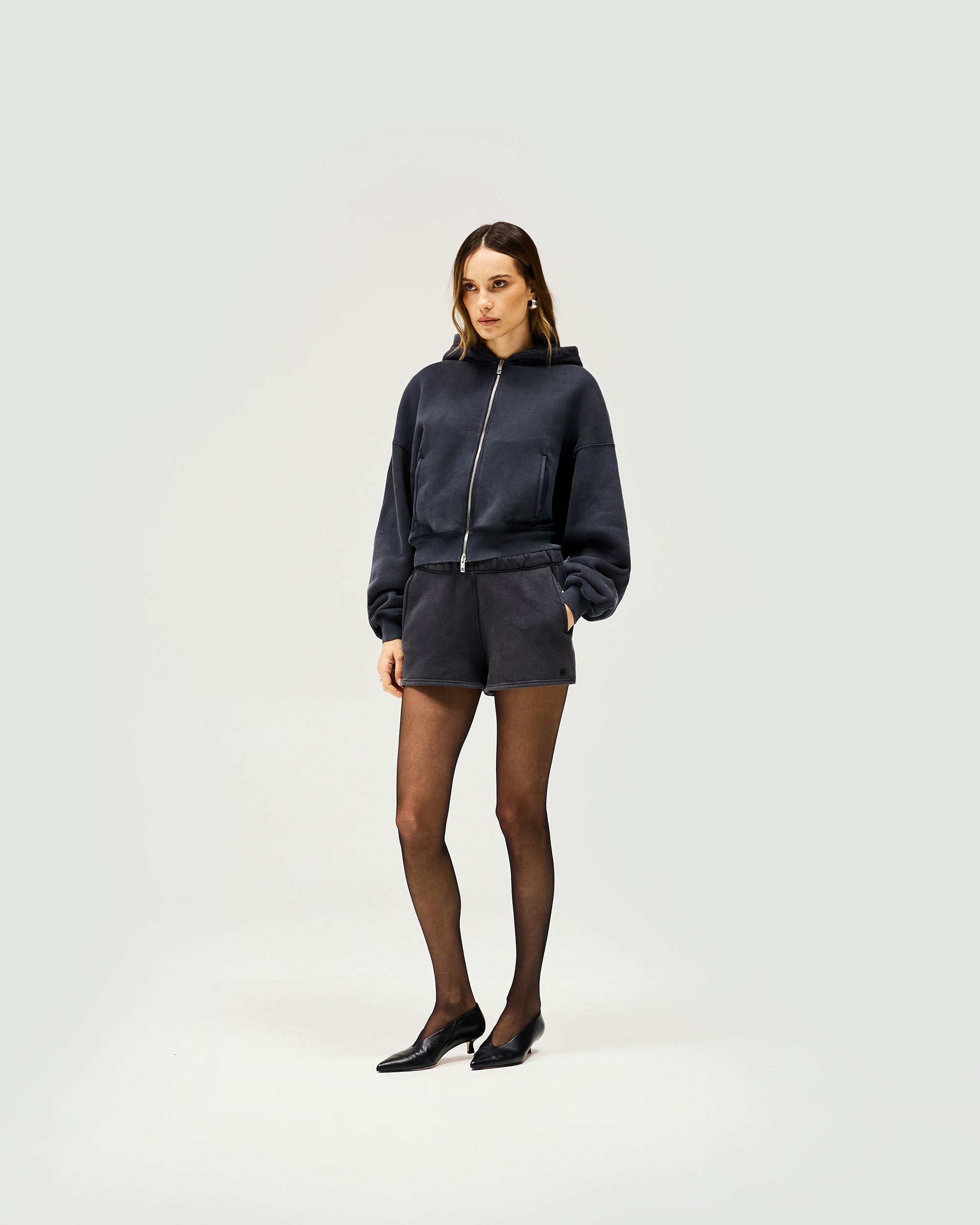 Woman wearing washed black mini sweat shorts on a plain white background | Initial Washed Shorts in Washed Black | Mini sweat shorts with elasticised waist and side pockets | Womens Initial Shorts | Represent Clo