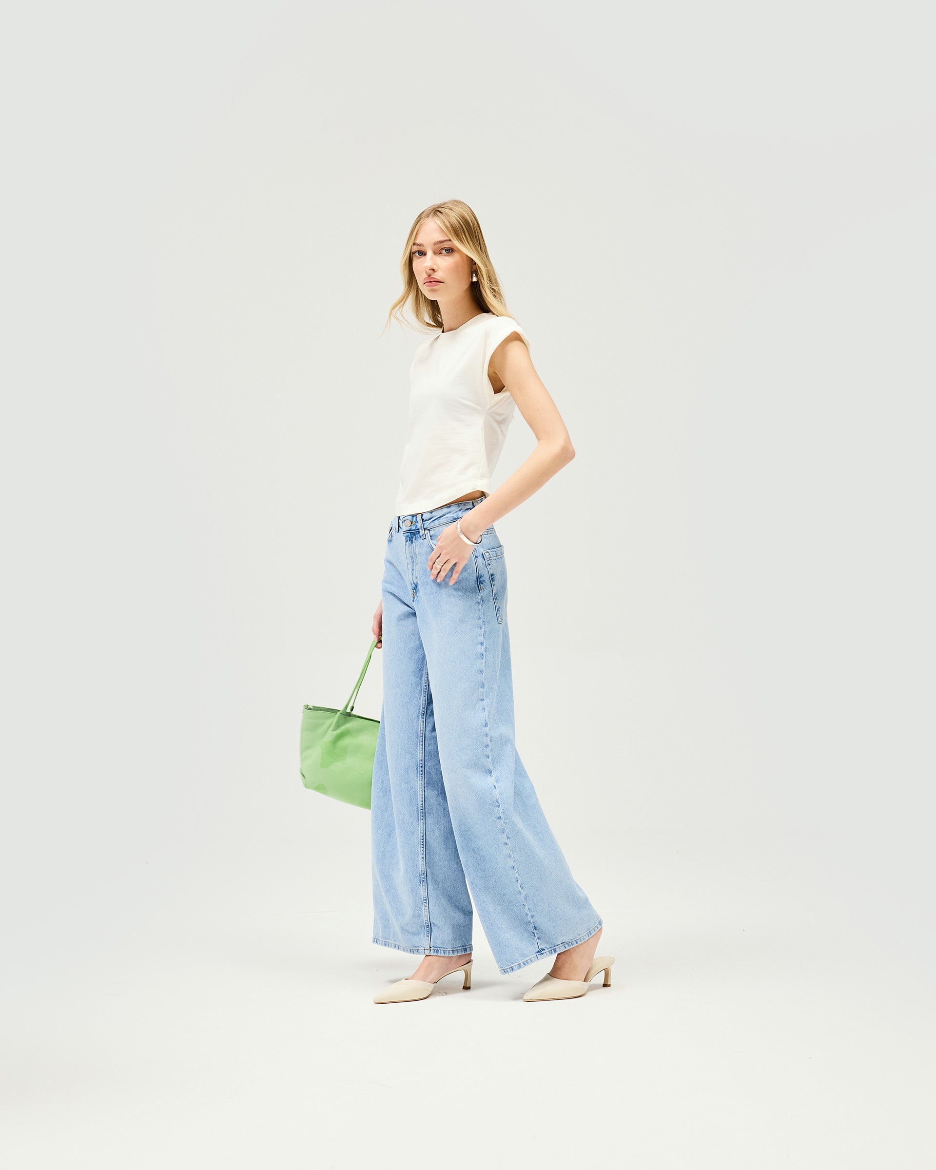 Woman wearing mid rise wide leg blue jeans on a plain white background | Mid Rise Wide Leg Jean in Washed Blue | Wide leg fit jeans with leather patch and nickel rivets | Womens SS25 Jeans | Represent Clo