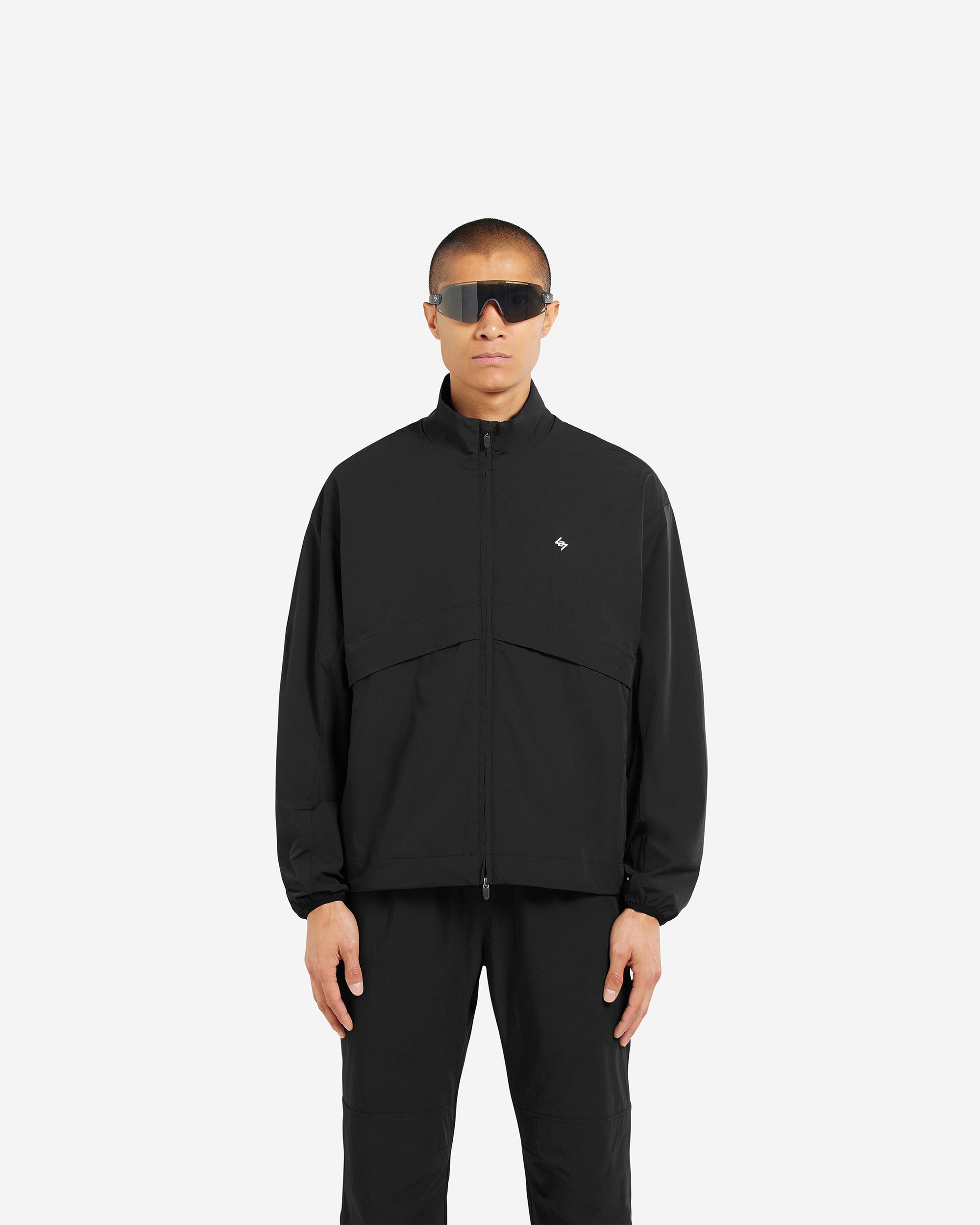 Man wearing a black track jacket on a plain white background | Team 247 Track Jacket in Black | Oversized track jacket with 4-way stretch nylon and technical mesh lining | 247 Outerwear | Represent Clo
