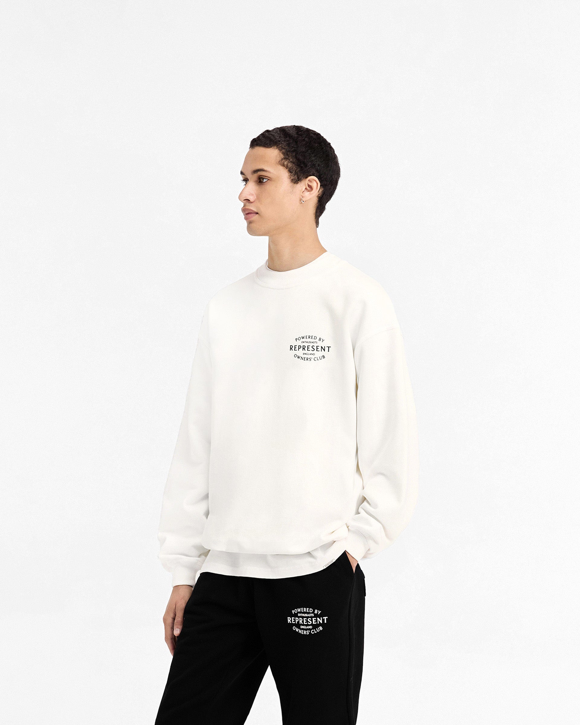 Man wearing a white sweater on a plain white background | Represent Owners Club Stamp Sweater in Flat White | Oversized fit cotton sweater with ribbed details | Owners Club Sweaters | Represent Clo