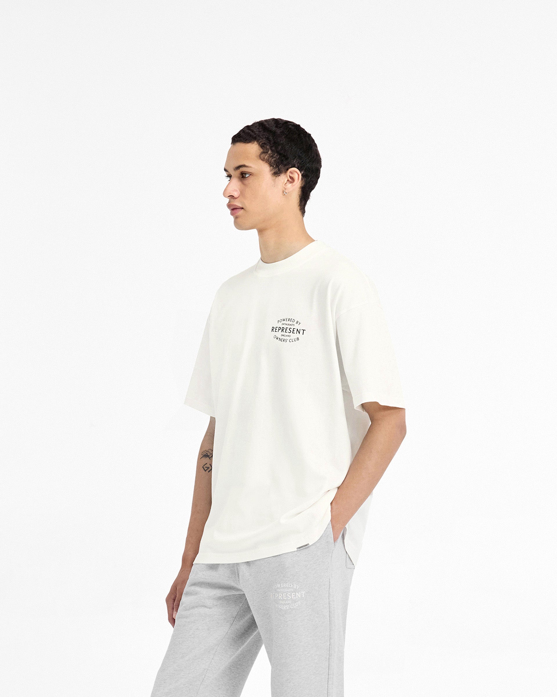 Man wearing a white t-shirt on a plain white background | Represent Owners Club Stamp T-Shirt in Flat White | Oversized fit t-shirt with metal bar logo and stamp branding | Owners Club T-Shirts | Represent Clo