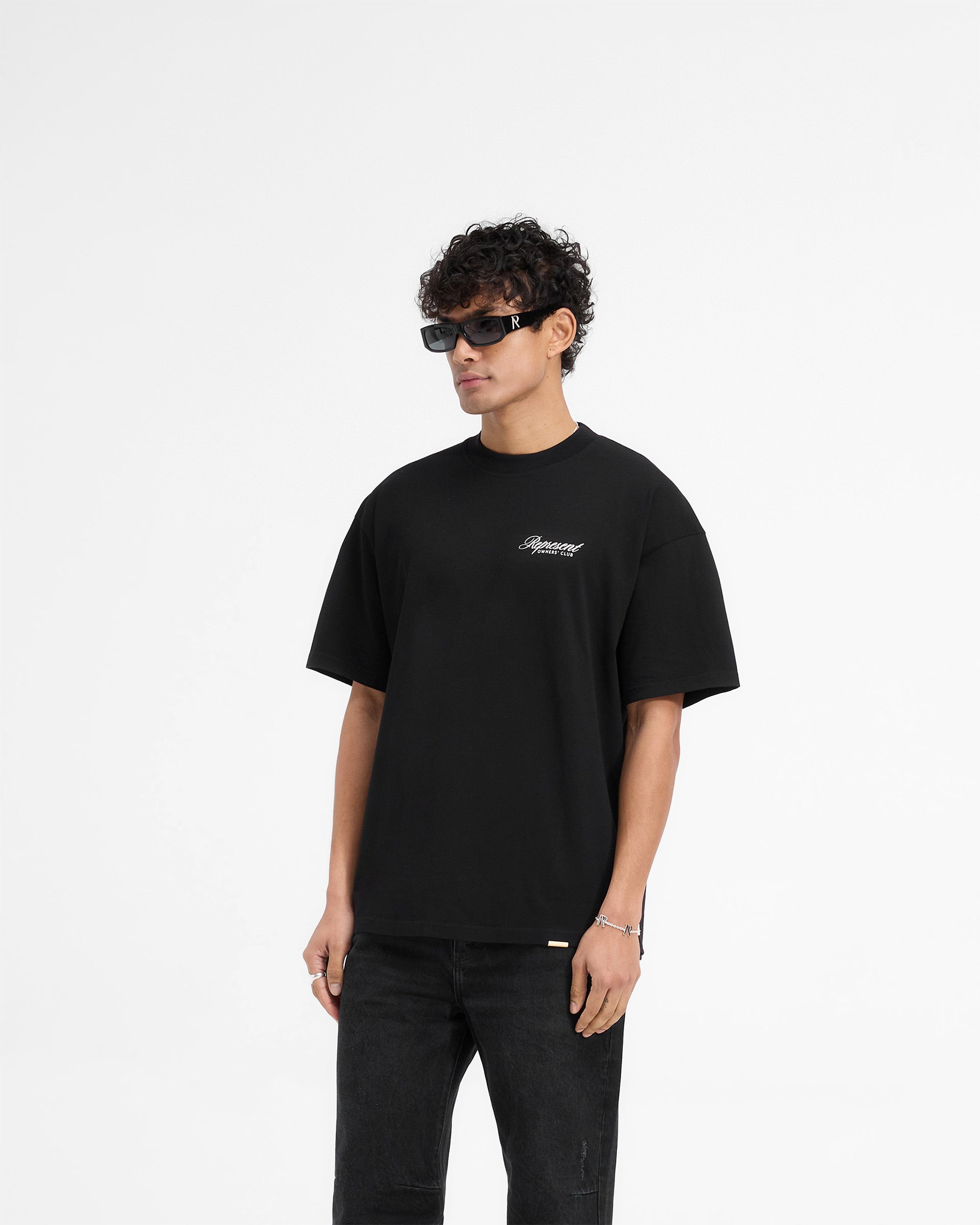 Man wearing a black t-shirt on a plain white background | Represent X Harrods Bear Owners Club T-Shirt in Jet Black | Oversized fit t-shirt with Harrods bear graphic and gold detailing | Exclusives T-Shirts | Represent Clo