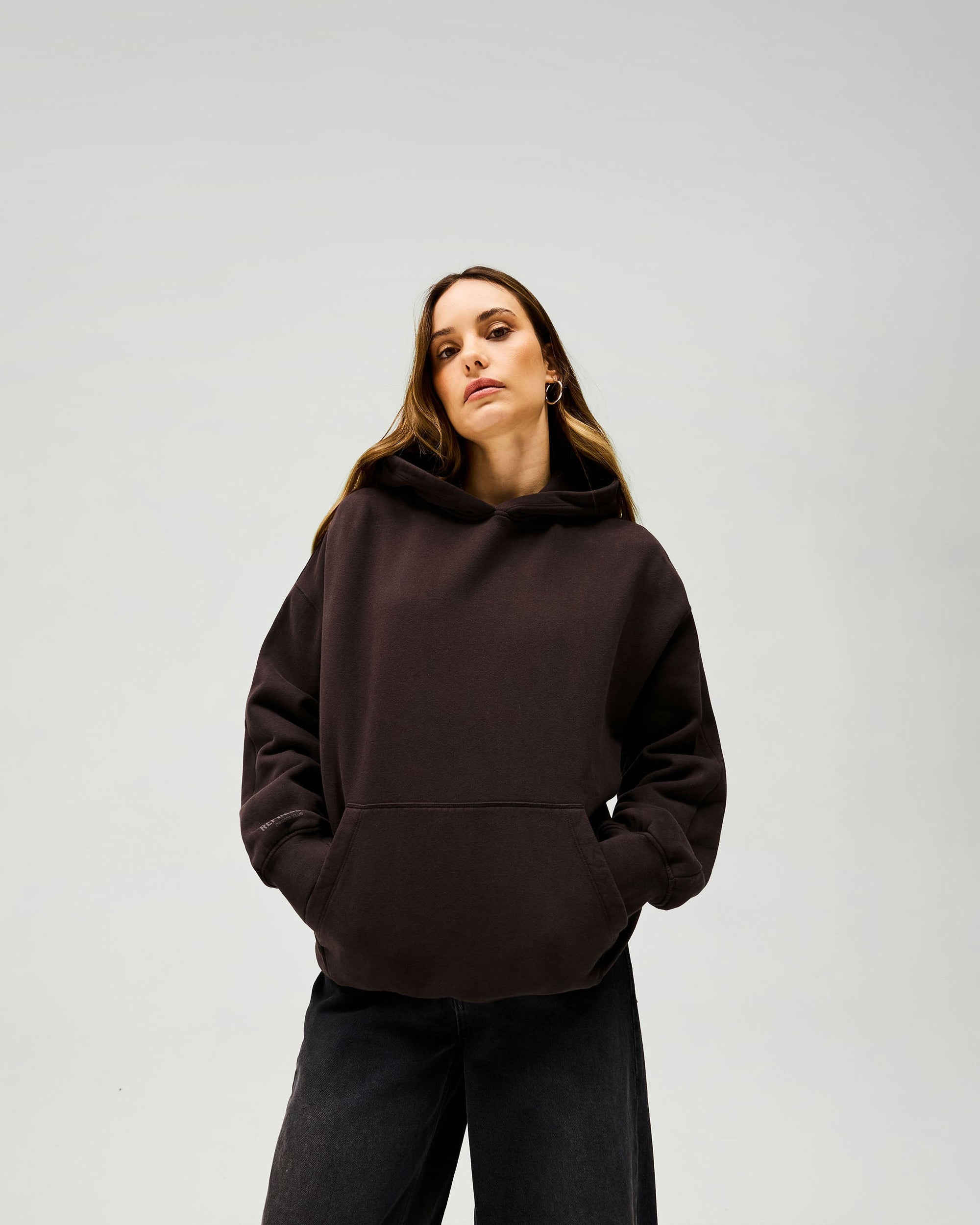 Woman wearing an oversized brown hoodie on a plain white background | Owners Club Boyfriend Hoodie in Black Coffee | Oversized hoodie with tonal puff print branding | Womens Owners Club Hoodies | Represent Clo