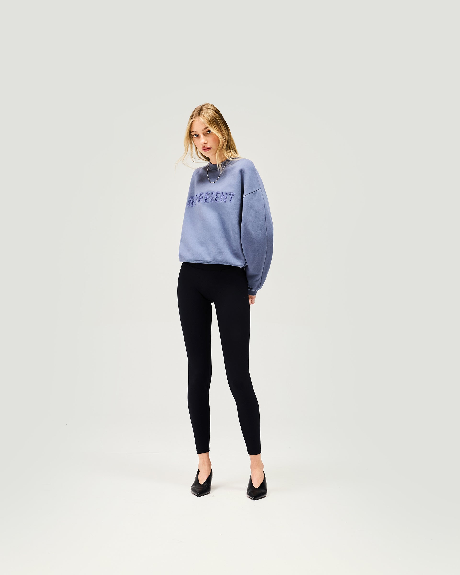 Woman wearing a blue sweater on a plain white background | Owners Club Sweater in Steel Blue | Relaxed crew neck sweater in soft cotton fleece | Womens Owners Club Sweaters | Represent Clo