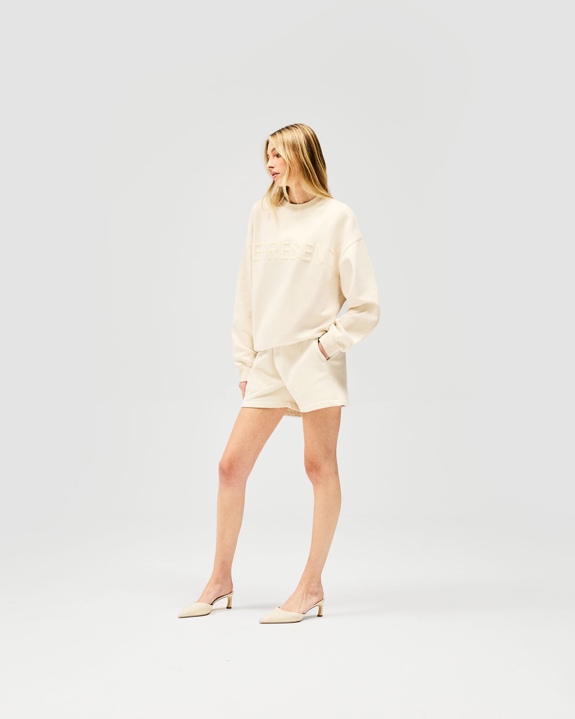 Woman wearing oat milk coloured shorts on a plain white background | Owners Club Short in Oat Milk | Classic sweat mini shorts in brushed cotton fleece | Womens Owners Club Shorts | Represent Clo