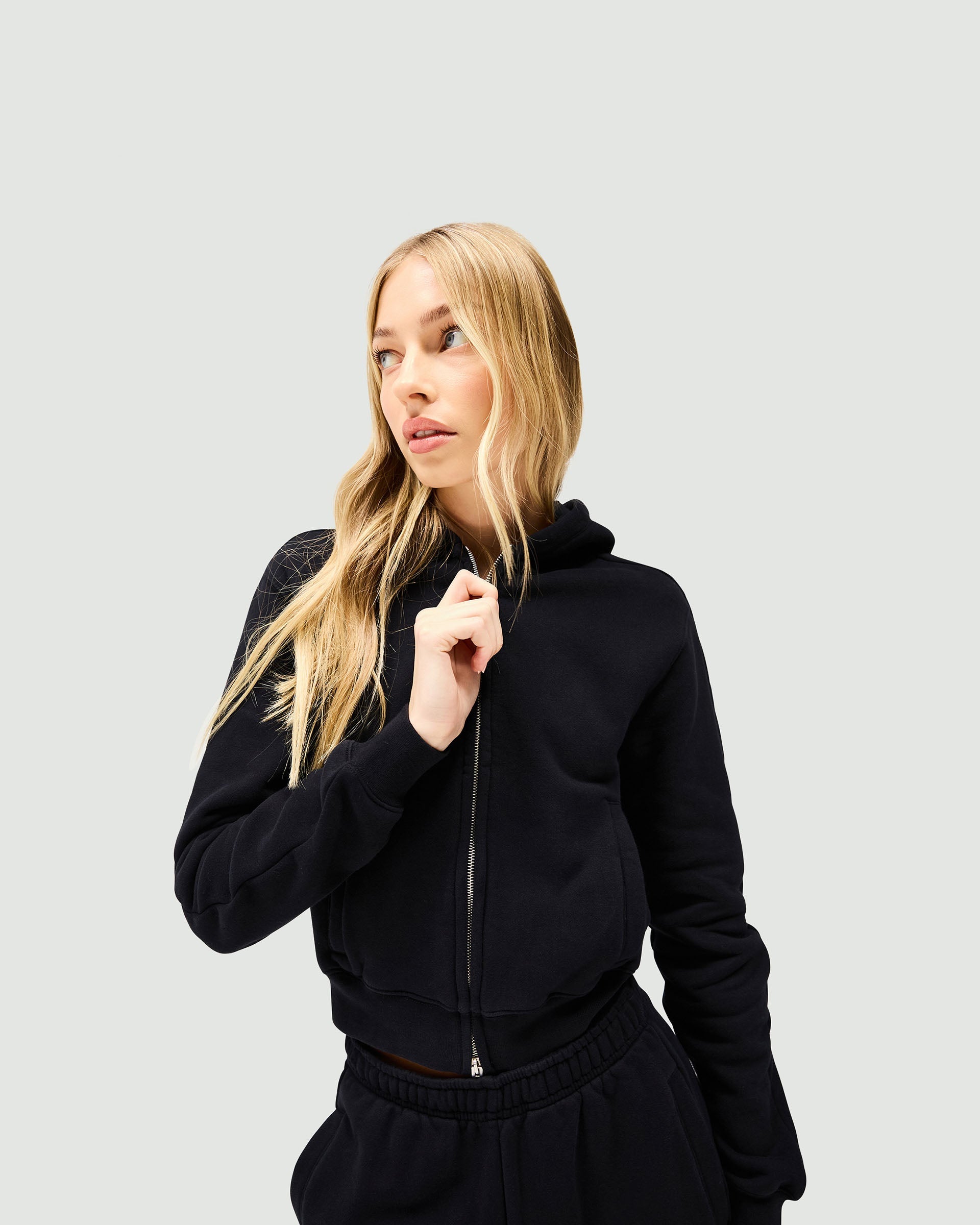 Woman wearing a black slim fit zip hoodie on a plain white background | Owners Club Slim Zip Hoodie in Jet Black | Cropped slim fit hoodie with double ended zipper | Womens Owners Club Hoodies | Represent Clo