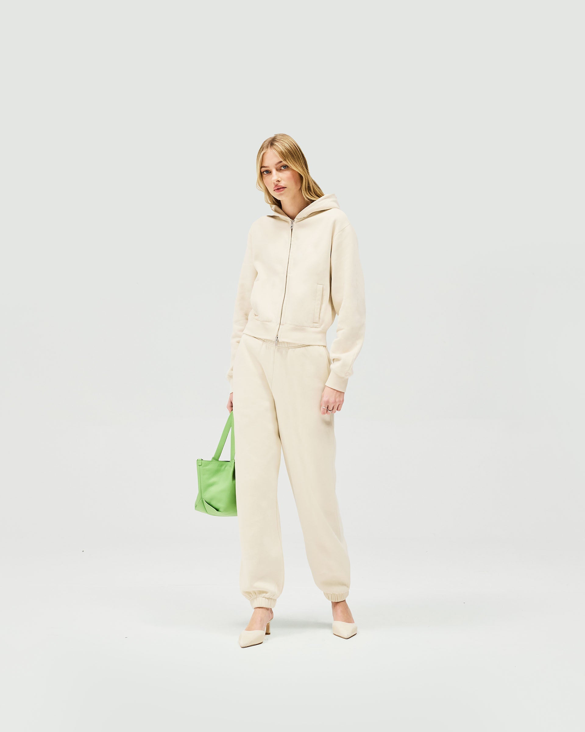 Woman wearing a slim fit oat milk hoodie on a plain white background | Owners Club Slim Zip Hoodie in Oat Milk | Cropped slim fit zip hoodie with double ended metal zipper | Womens Owners Club Hoodies | Represent Clo