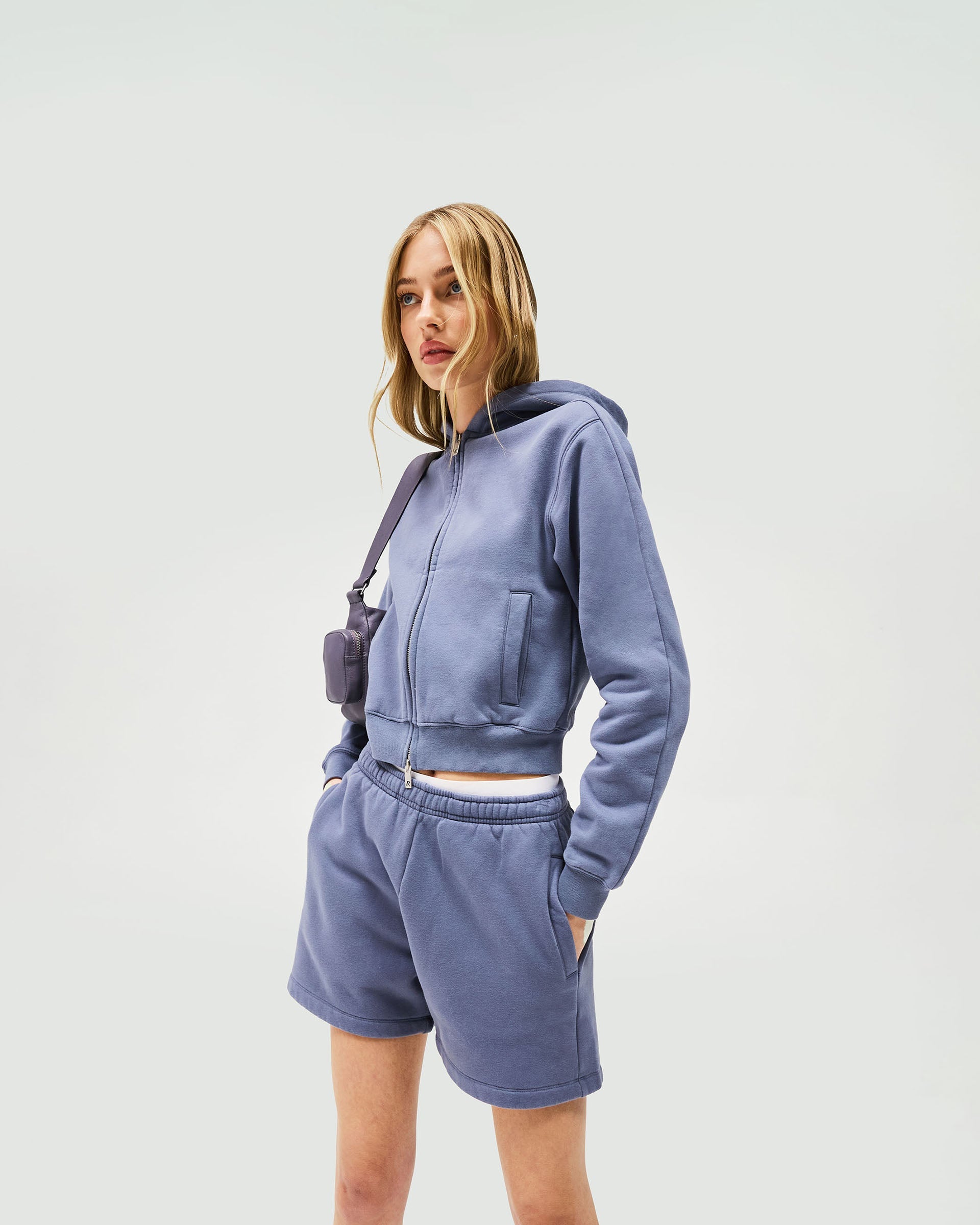 Woman wearing a slim fit blue hoodie on a plain white background | Owners Club Slim Zip Hoodie in Steel Blue | Slim fit zip through hoodie with tonal puff print | Womens Owners Club Hoodies | Represent Clo