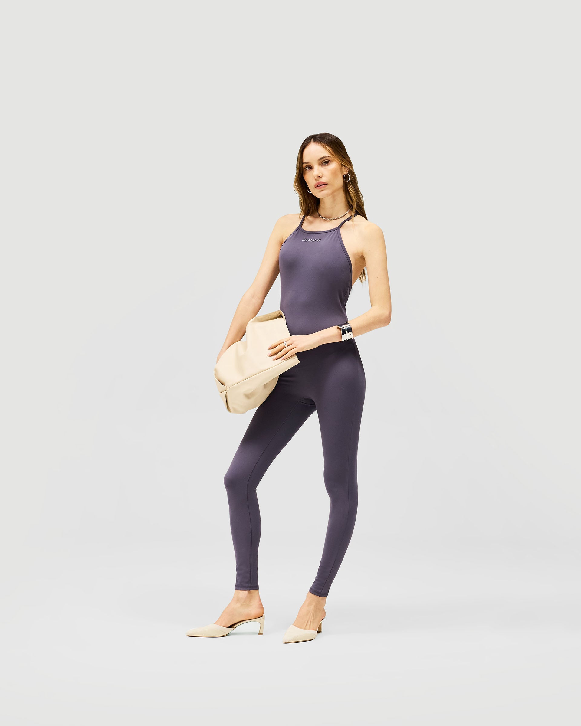 Woman wearing a grey unitard on a plain white background | Owners Club Unitard in Grey | Full length sculpted fit unitard with contouring crossback | Womens Jumpsuits | Represent Clo