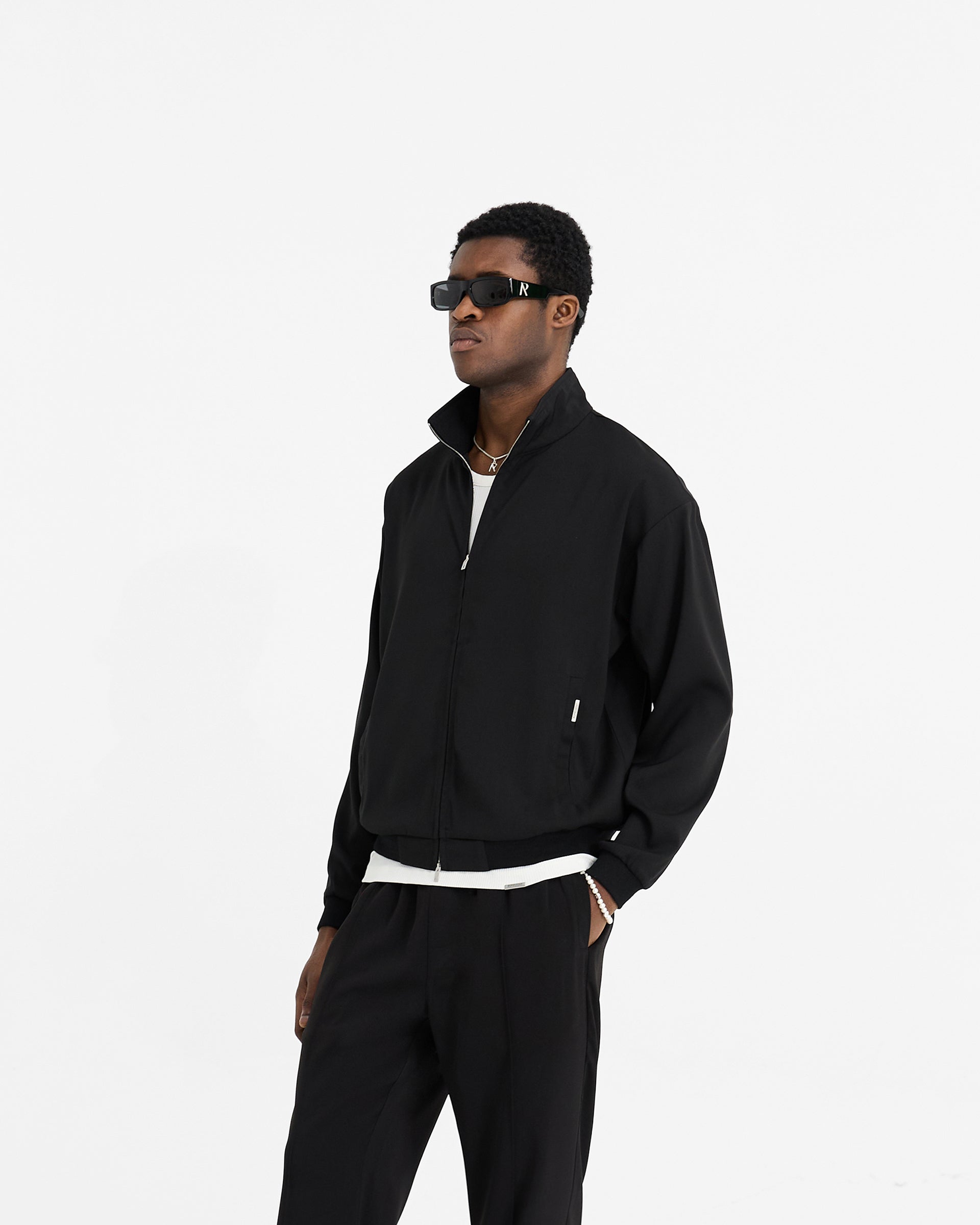 Back product image of a mens black track jacket on a plain white background | Initial Track Jacket in Black | Slightly oversized track jacket with branded RiRi zip closure | Initial Outerwear | Represent Clo