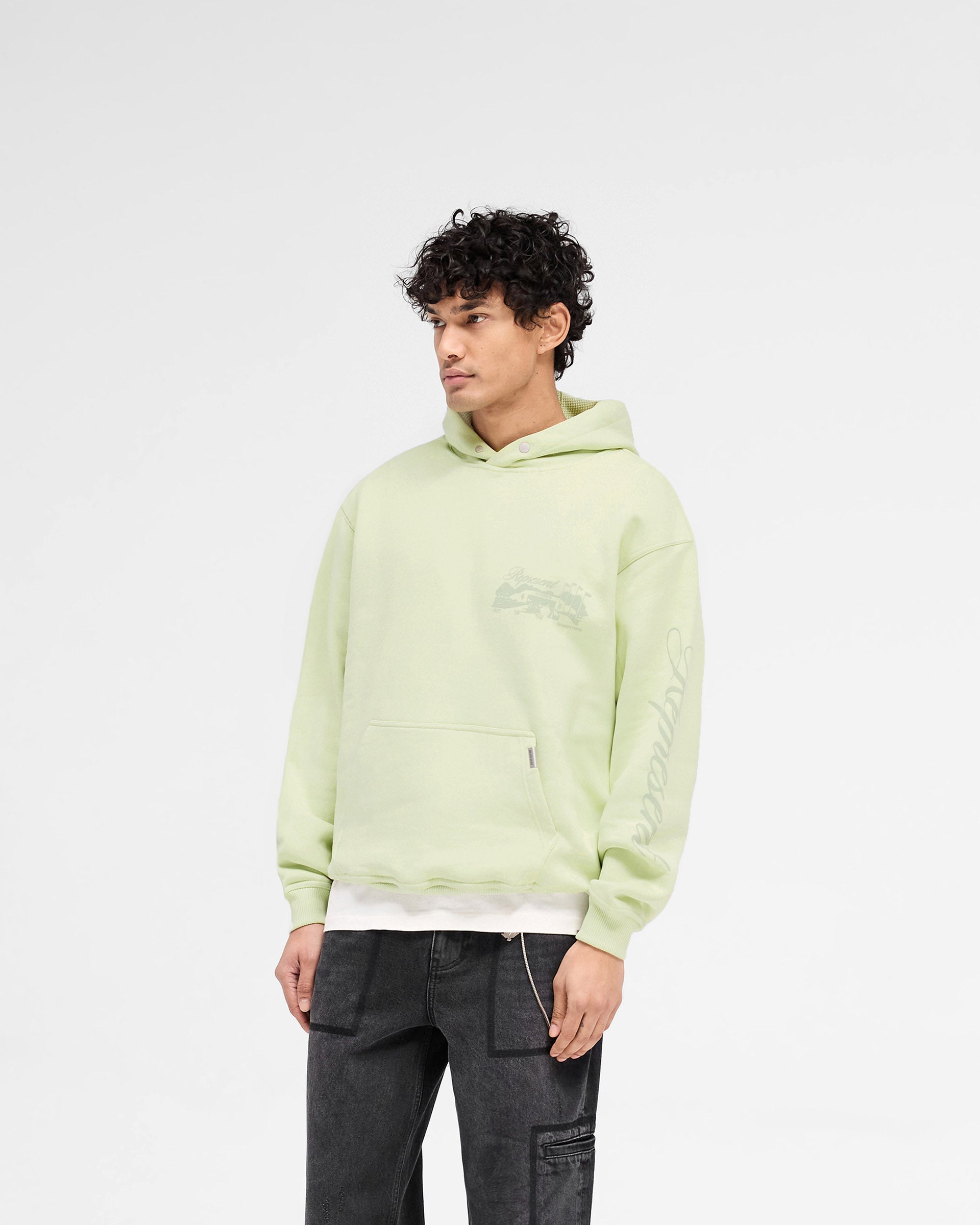 Man wearing a green hoodie on a plain white background | Raceway Hoodie in Matcha | Slightly oversized hoodie with puff print and sleeve detail | SS25 Hoodies | Represent Clo