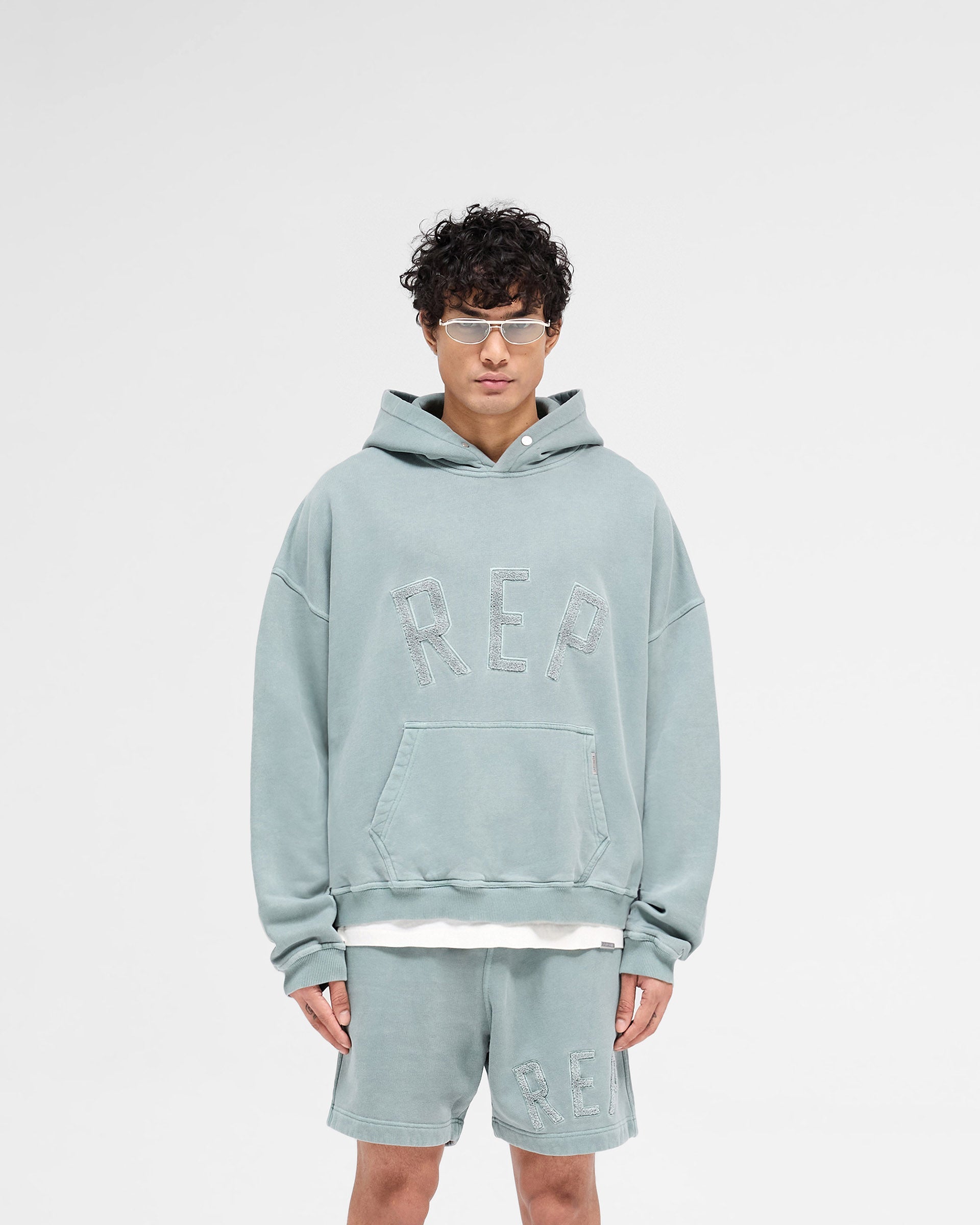 Man wearing a green hoodie on a plain white background | Rep Applique Hoodie in Forest Green | Boxy fit hoodie with textured applique | SS25 Hoodies | Represent Clo