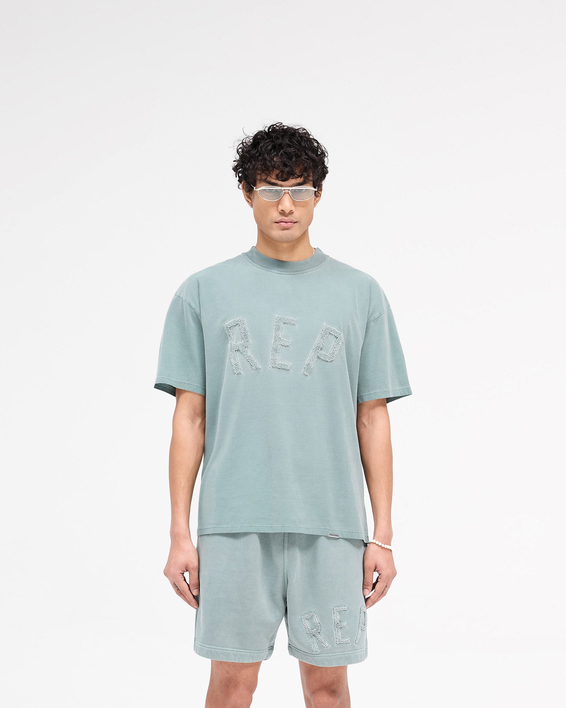 Man wearing a green t-shirt on a plain white background | Rep Applique T-Shirt in Forest Green | Slightly oversized t-shirt with textured Rep applique | SS25 T-Shirts | Represent Clo