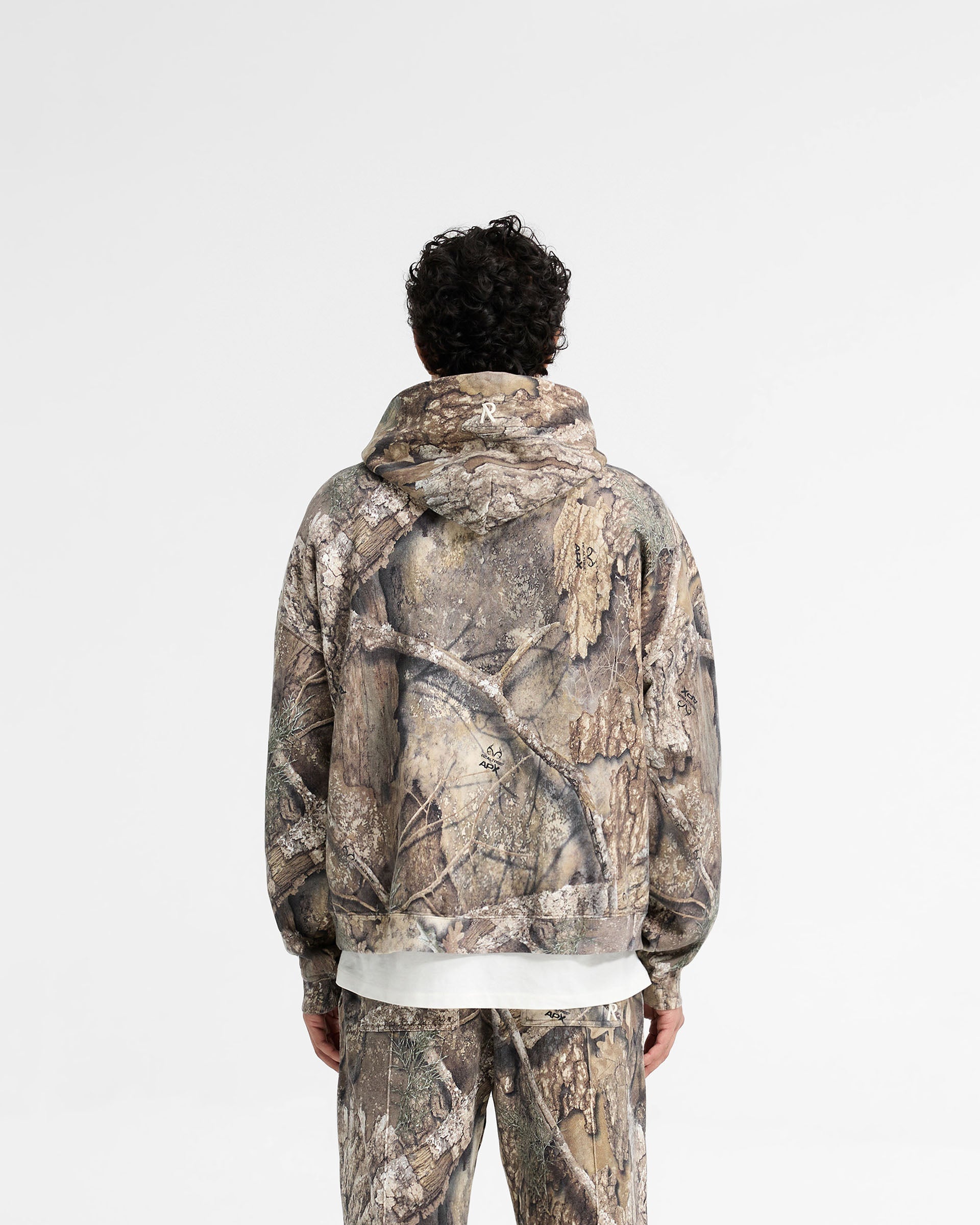 Man wearing a camo hoodie on a plain white background | Realtree Camo Boxy Hoodie in Camo | Camouflage design hoodie with dropped shoulders | SS25 Hoodies | Represent Clo