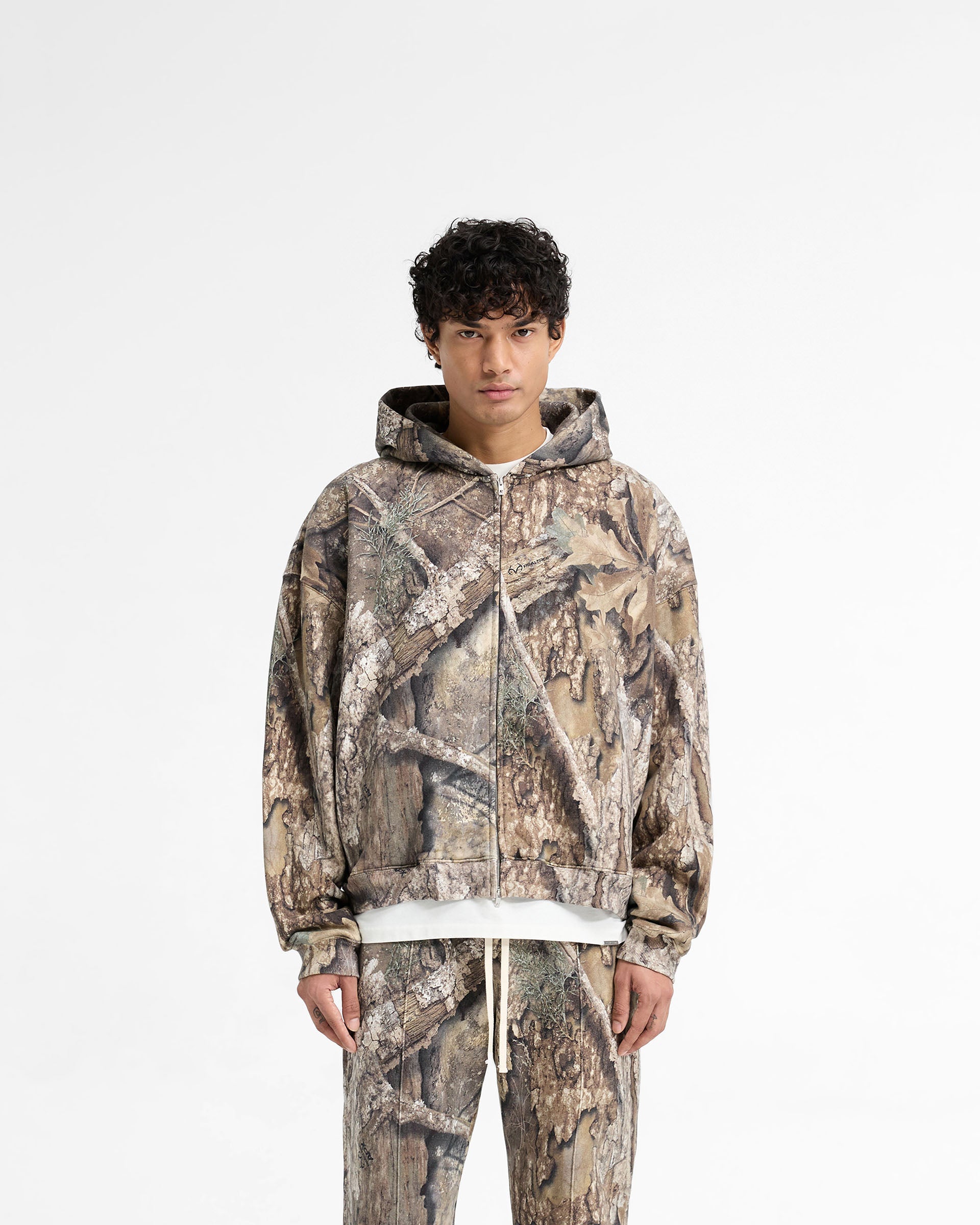 Man wearing a camo hoodie on a plain white background | Realtree Zip Up Camo Boxy Hoodie in Camo | Oversized boxy fit hoodie with double ended zip | SS25 Hoodies | Represent Clo