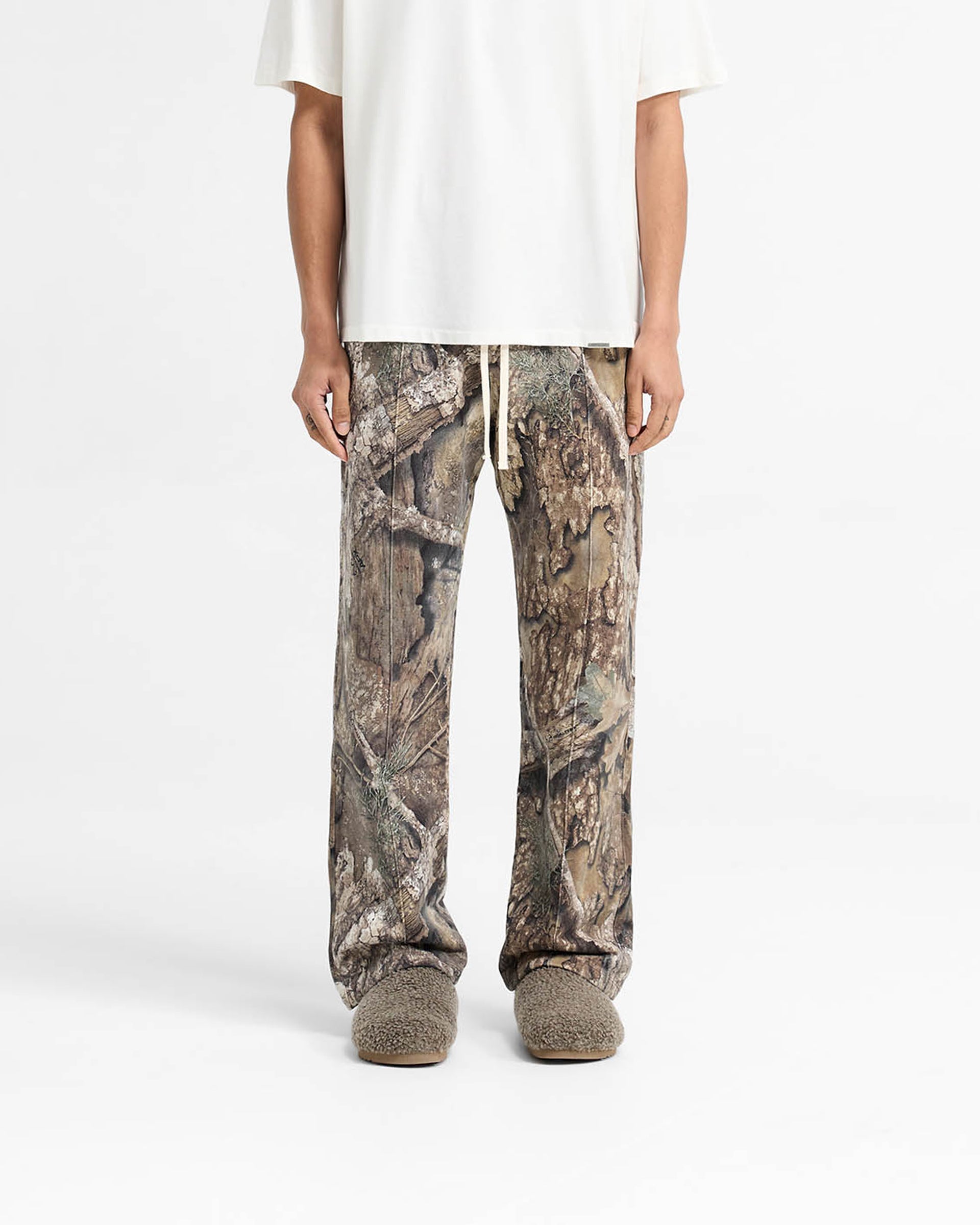 Man wearing camo pants on a plain white background | Realtree Camo Sweatpants in Camo | Wide leg sweatpants with elasticated waistband | SS25 Pants | Represent Clo