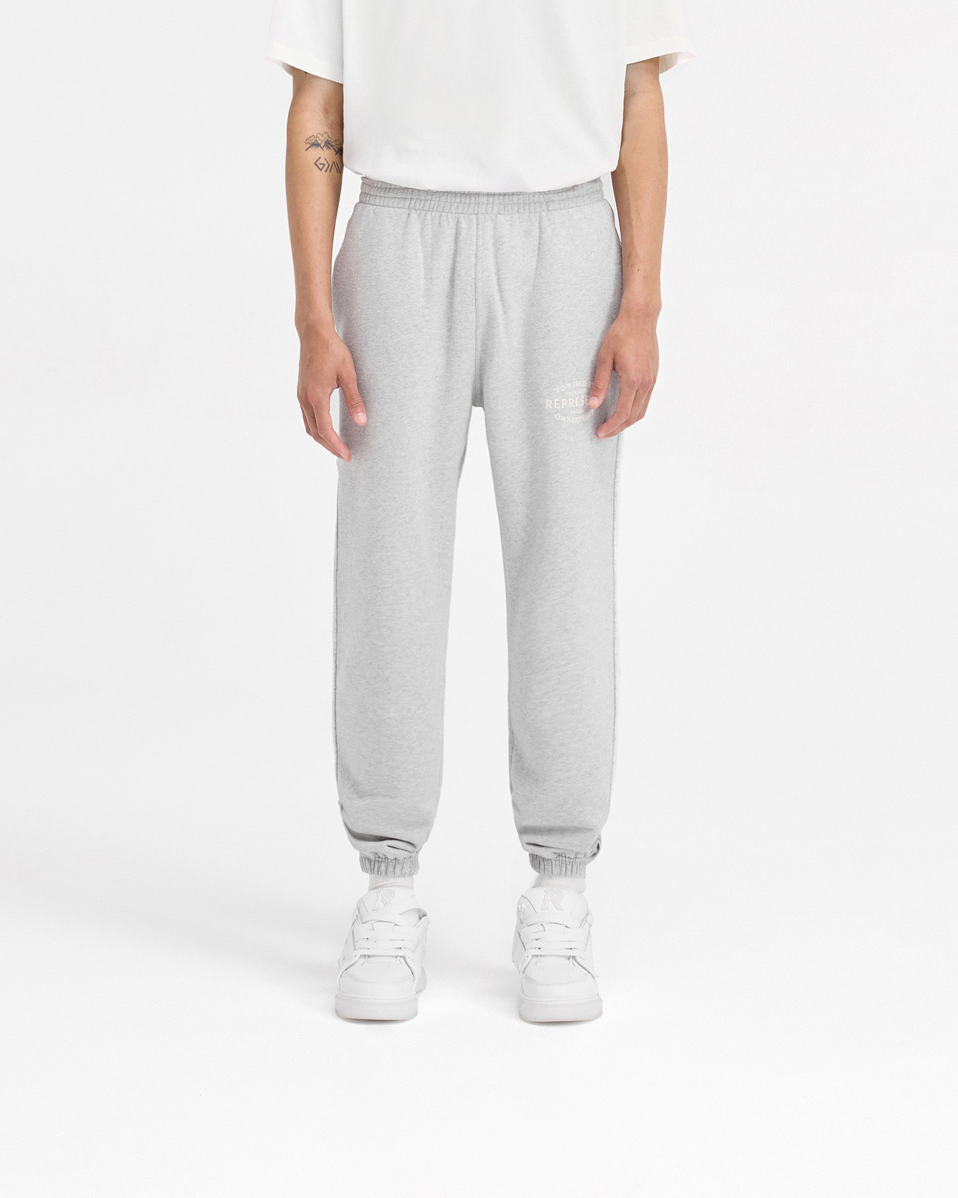 Man wearing ash grey sweatpants on a plain white background | Represent Owners Club Stamp Sweatpant in Ash Grey | Sweatpants with elasticated waistband and welt pockets | Owners Club Pants | Represent Clo