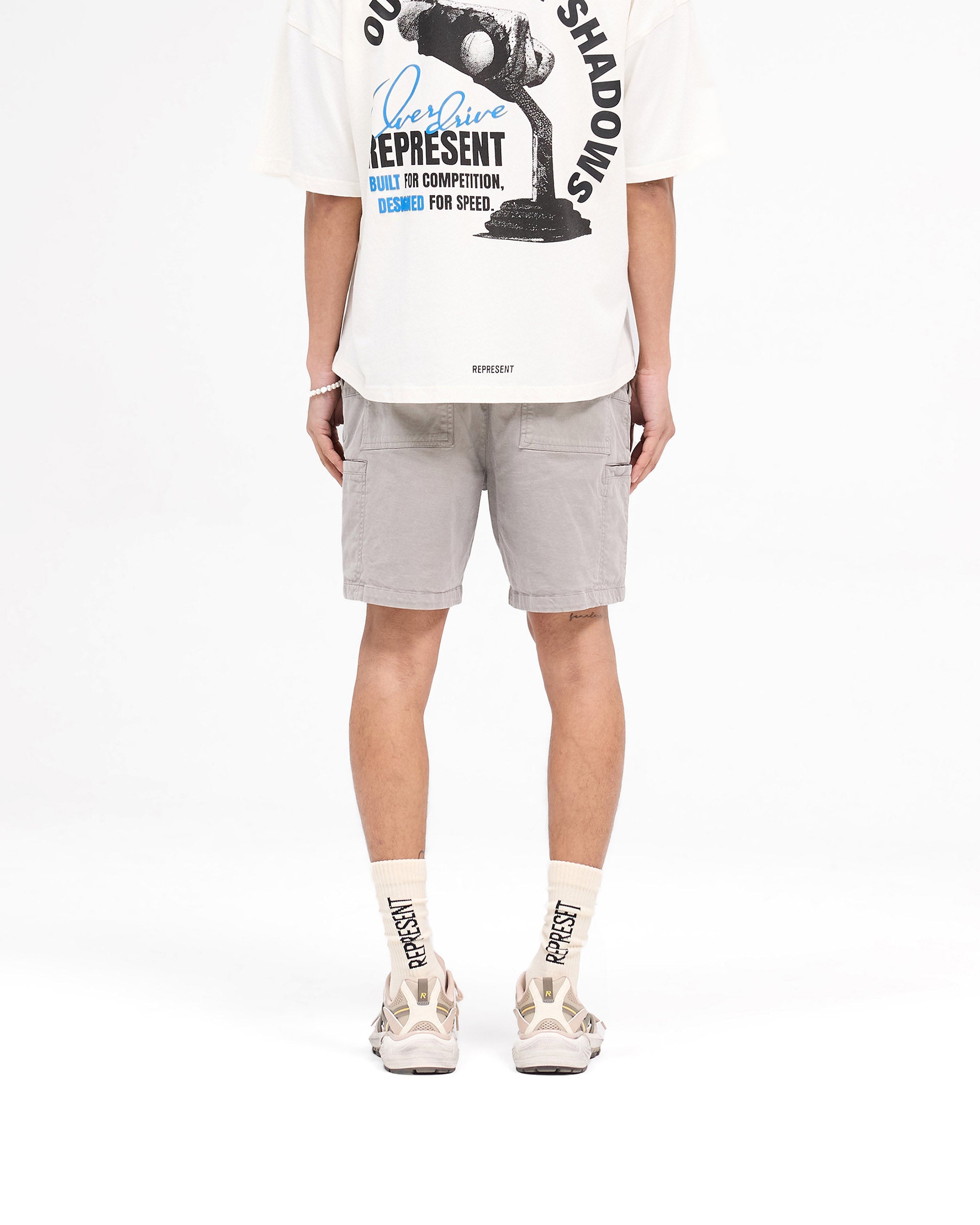 Man wearing mens grey cargo shorts on a plain white background | Season Cargo Short in Washed Taupe | Shorts with welt cargo and diagonal hand pockets | SS25 Shorts | Represent Clo