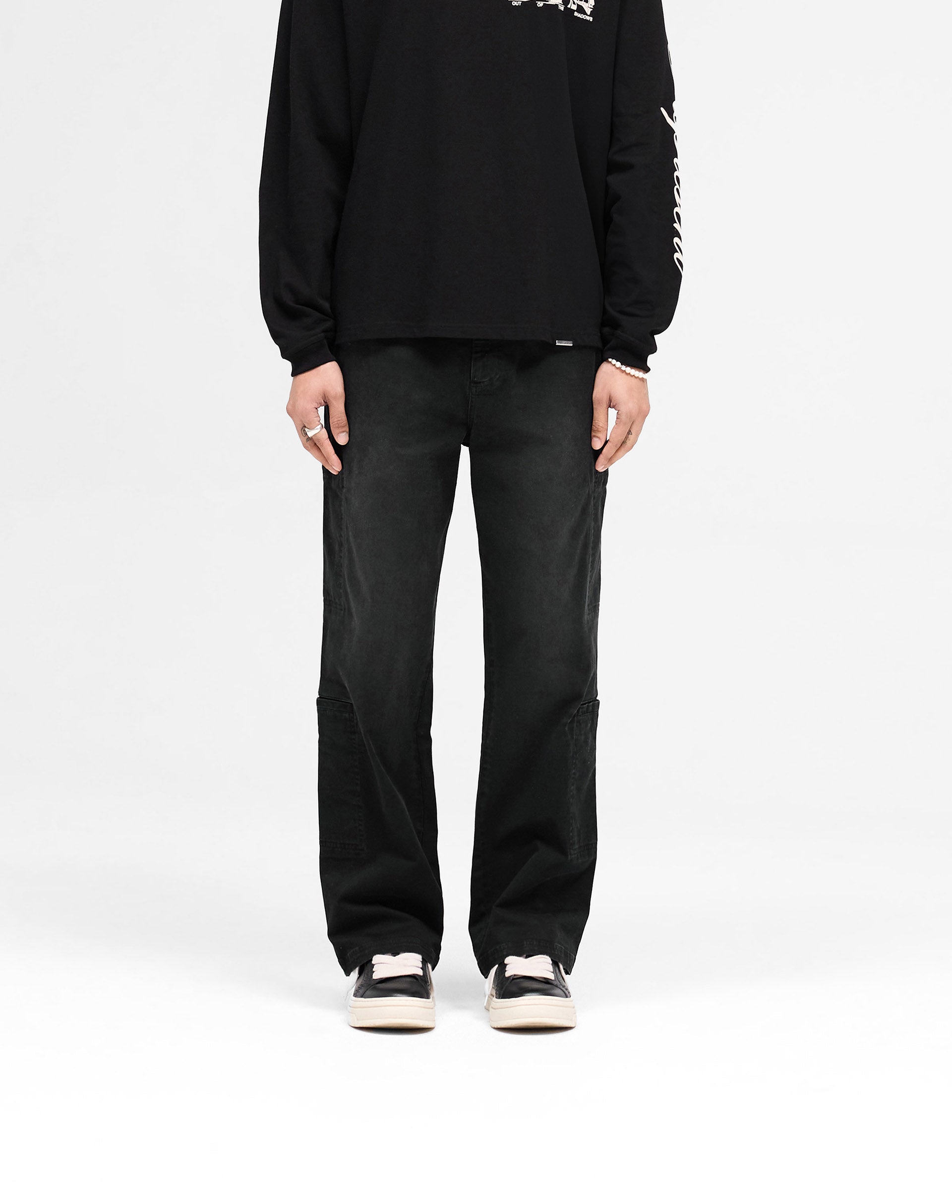 Man wearing black cargo pants on a plain white background | Season Cargo Pant in Jet Black | Cargo pants with eight pockets and brushed twill fabric | SS25 Pants | Represent Clo