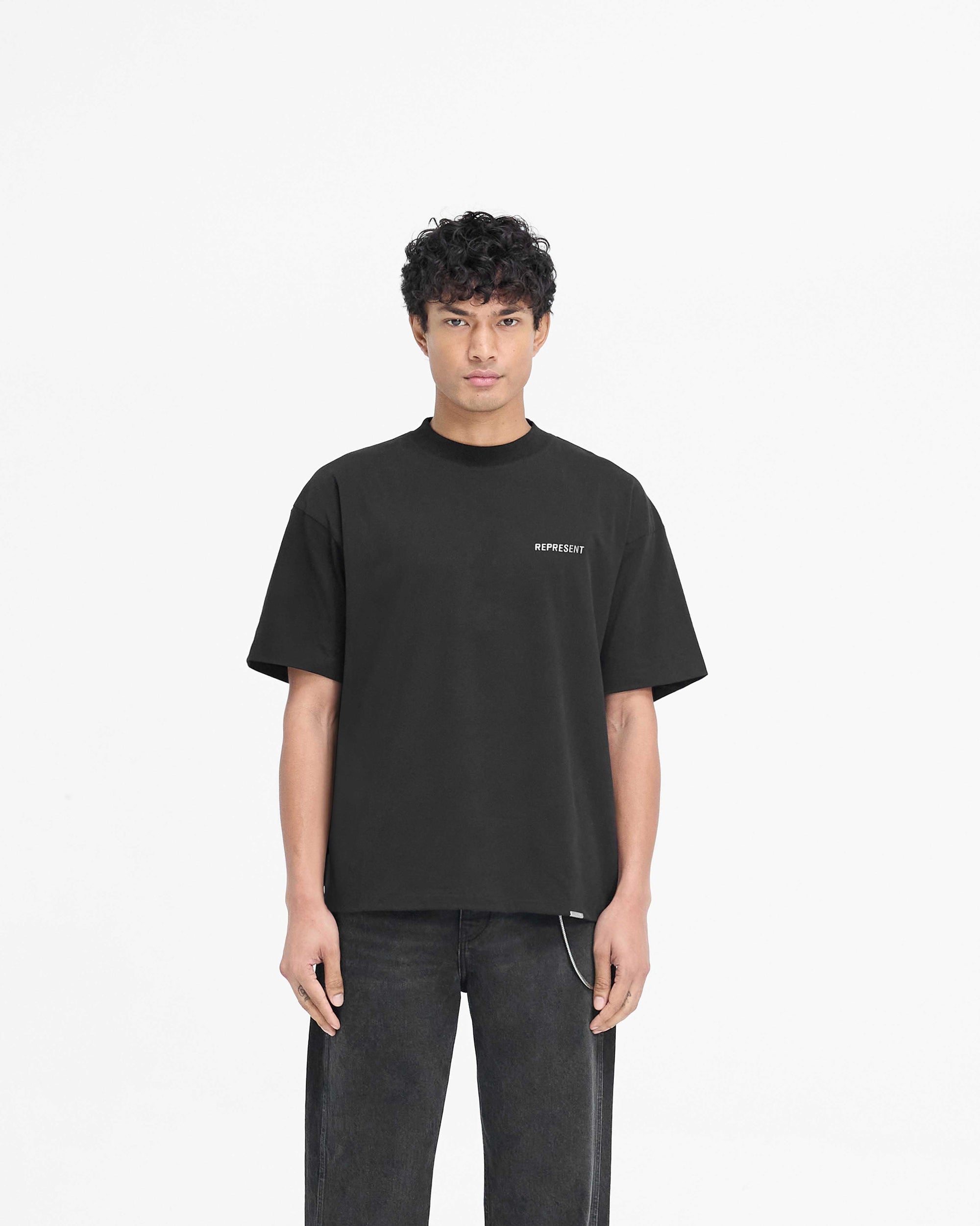 Man wearing a black t-shirt on a plain white background | Block Logo T-Shirt in Jet Black | Slightly oversized t-shirt with metal branding | PRE SS25 T-Shirts | Represent Clo