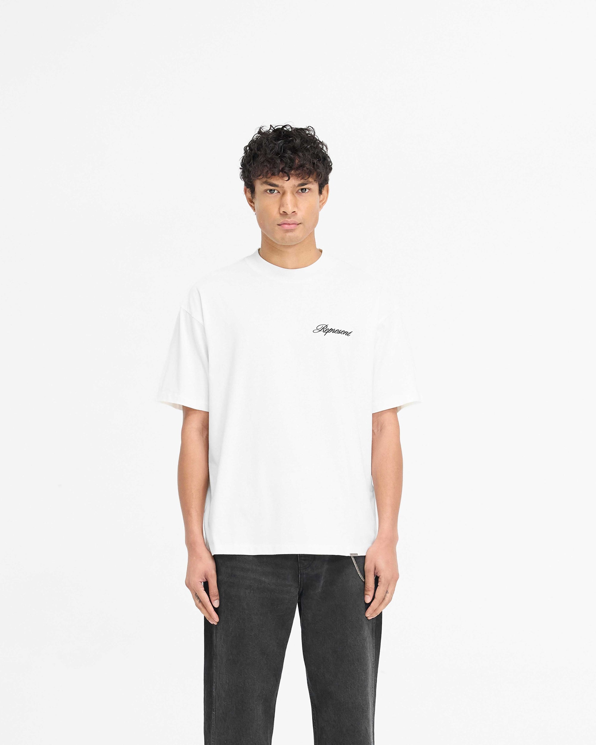 Man wearing a slightly oversized white t-shirt on a plain white background | Script Logo T-Shirt in Flat White | Jersey cotton t-shirt with high build embroidery | PRE SS25 T-Shirts | Represent Clo
