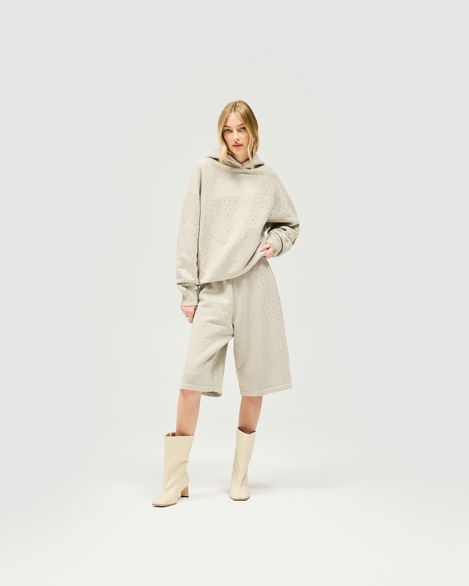 Woman wearing an oversized grey hoodie on a plain white background | Spark Hoodie in Storm | Slouchy hoodie with all over hotfix detailing | Womens SS25 Hoodies | Represent Clo