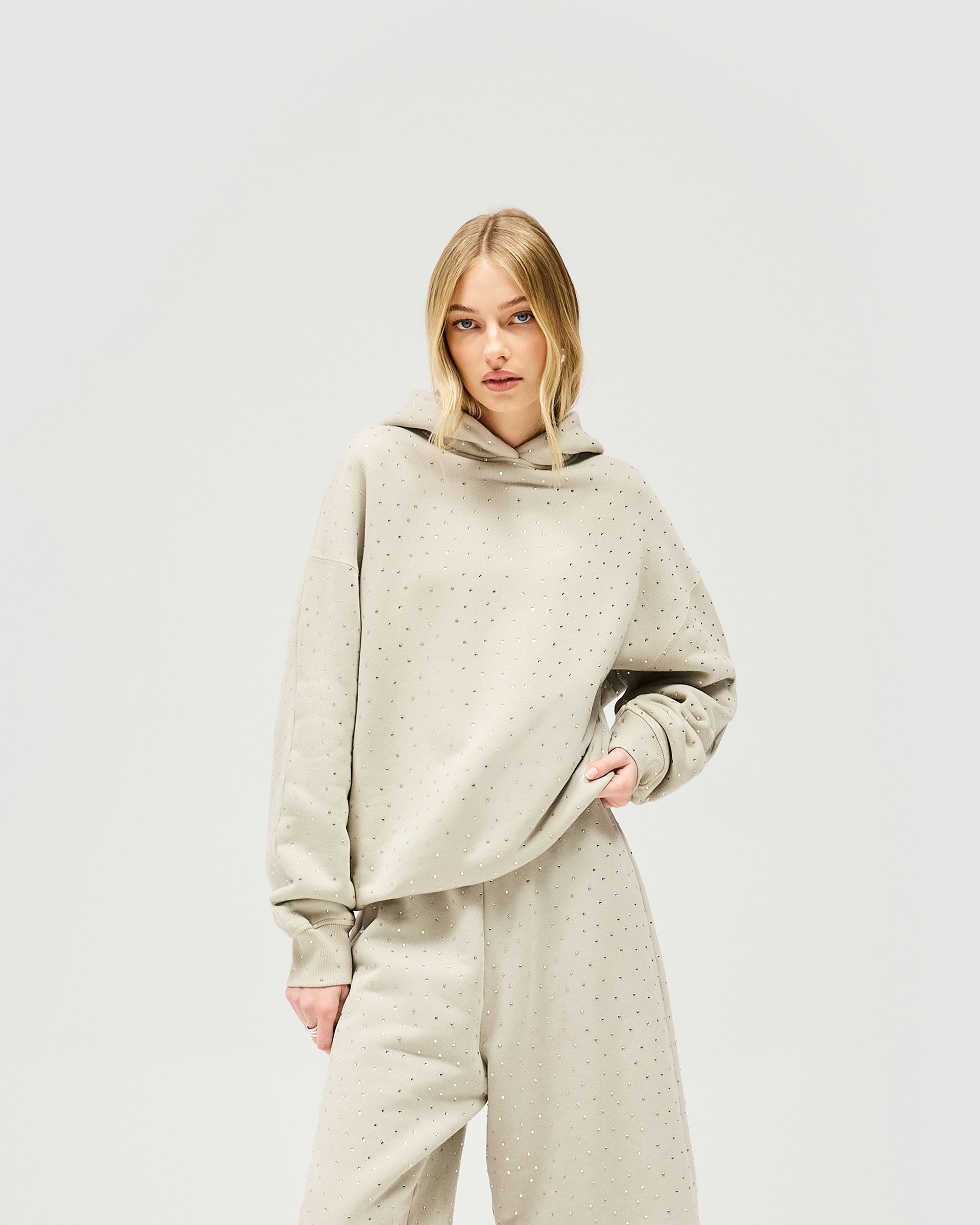 Woman wearing an oversized grey hoodie with acid wash on a plain white background | Spark Hoodie in Storm | Oversized hoodie with all over hotfix | Womens SS25 Hoodies | Represent Clo