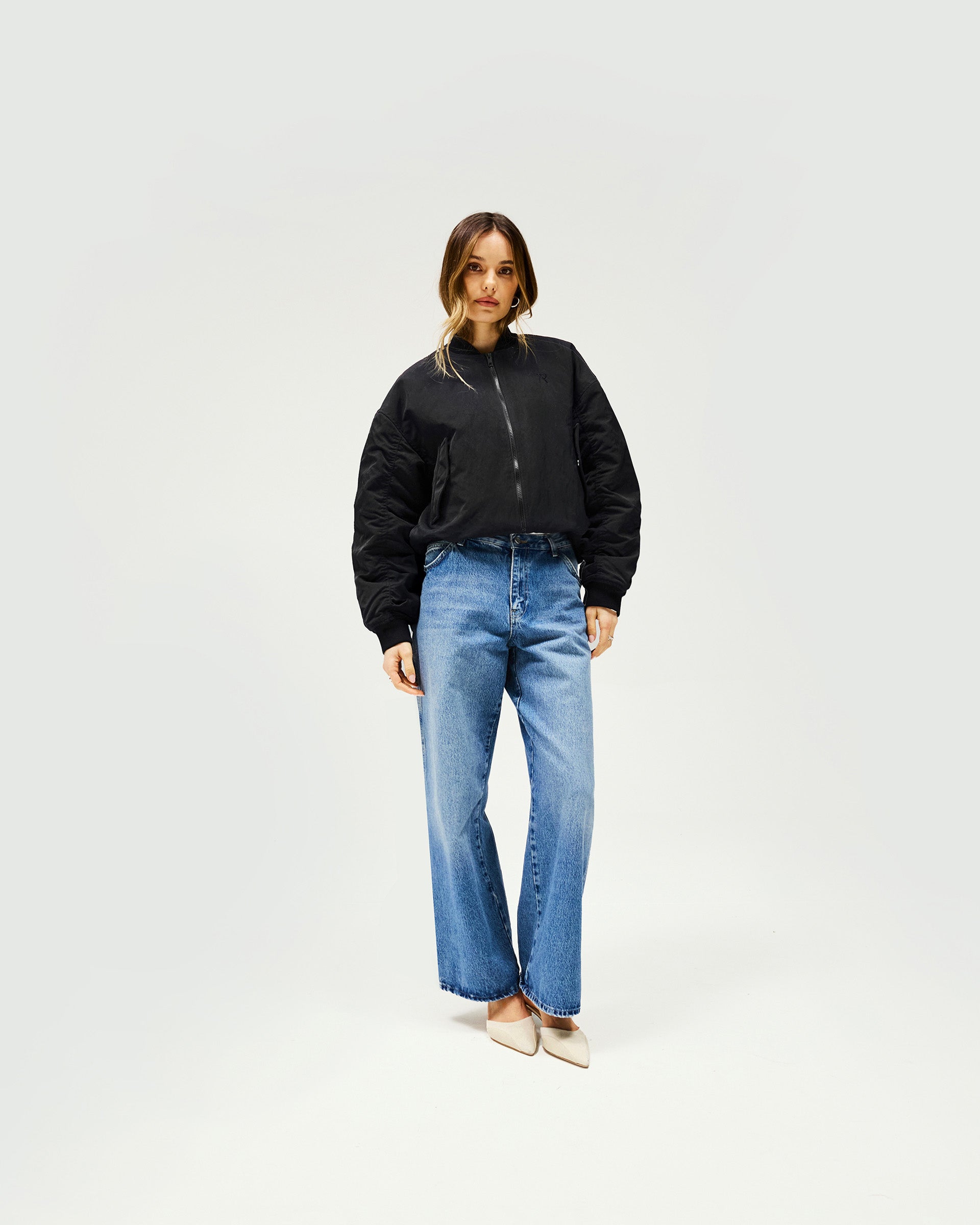 Woman wearing a black oversized bomber jacket on a plain white background | Subway Jacket in Jet Black | Nylon bomber with embroidered logo and ribbed cuffs | Womens SS25 Outerwear | Represent Clo