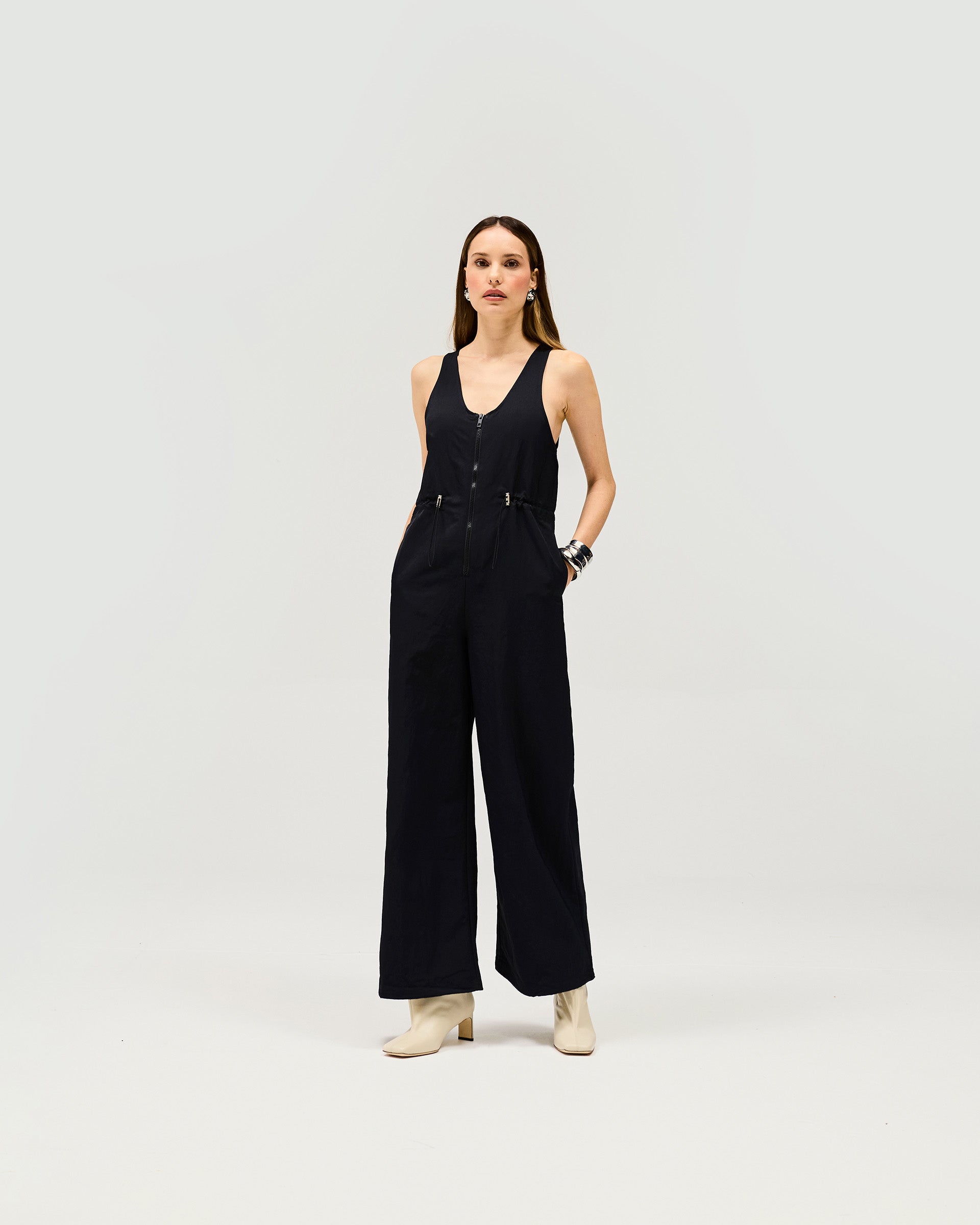 Woman wearing a black jumpsuit on a plain white background | Subway Jumpsuit in Jet Black | Sleeveless jumpsuit with drawstring waist and zip front | Womens SS25 Jumpsuits | Represent Clo