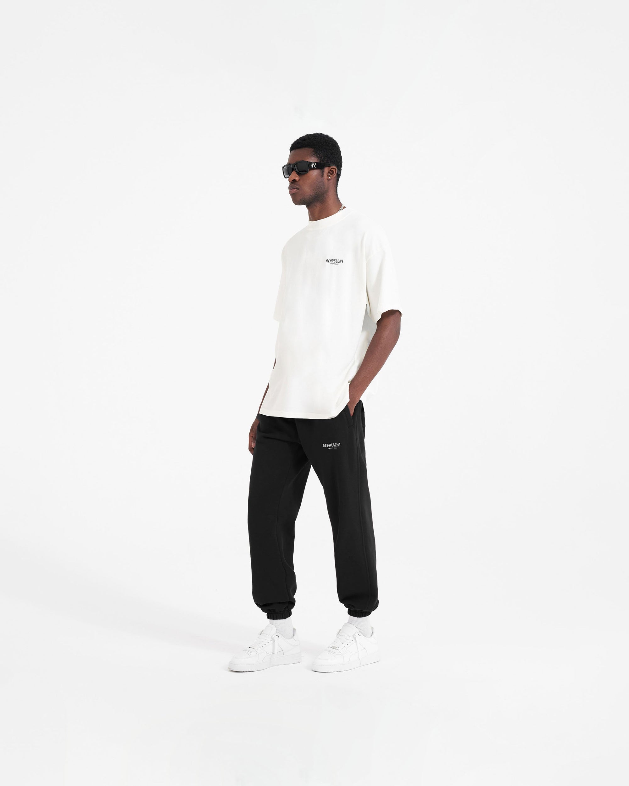 Man wearing black sweatpants on a plain white background | Represent Owners Club Sweatpant in Black | Sweatpants with elasticated waistband and logo detail | Owners Club Pants | Represent Clo