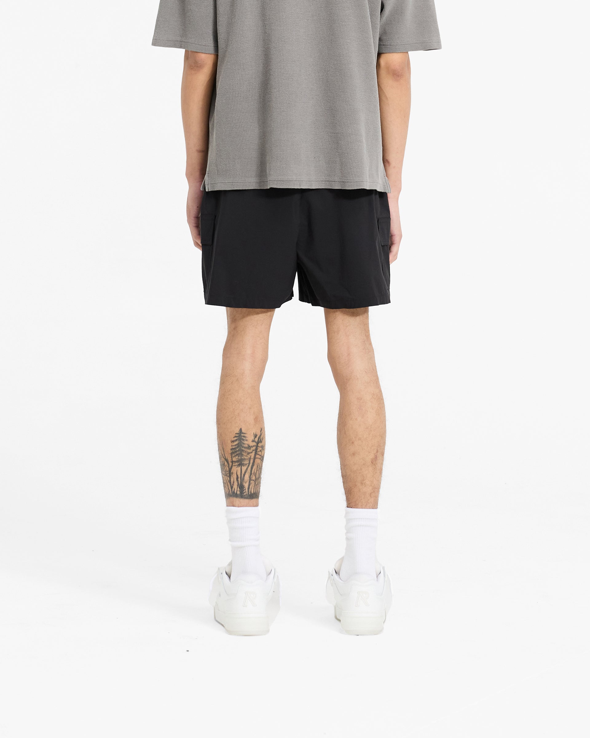 Man wearing black swim shorts on a plain white background | Cargo Swim Shorts in Black | Swim shorts with cargo pockets and buckle adjusters | SC24 Shorts | Represent Clo