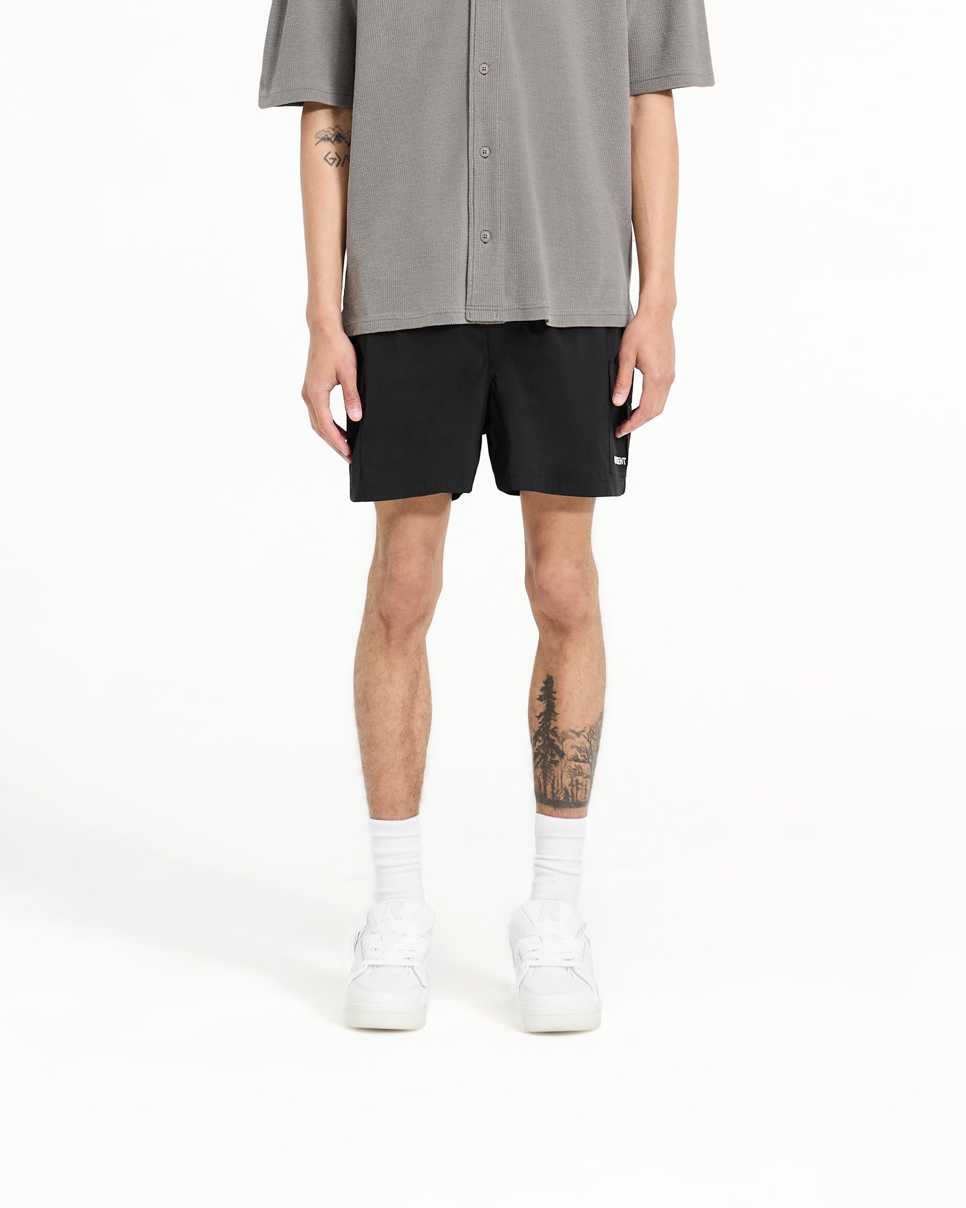 Man wearing black cargo swim shorts on a plain white background | Cargo Swim Shorts in Jet Black | Swim shorts with cargo flap pockets and buckle adjusters | SC24 Shorts | Represent Clo