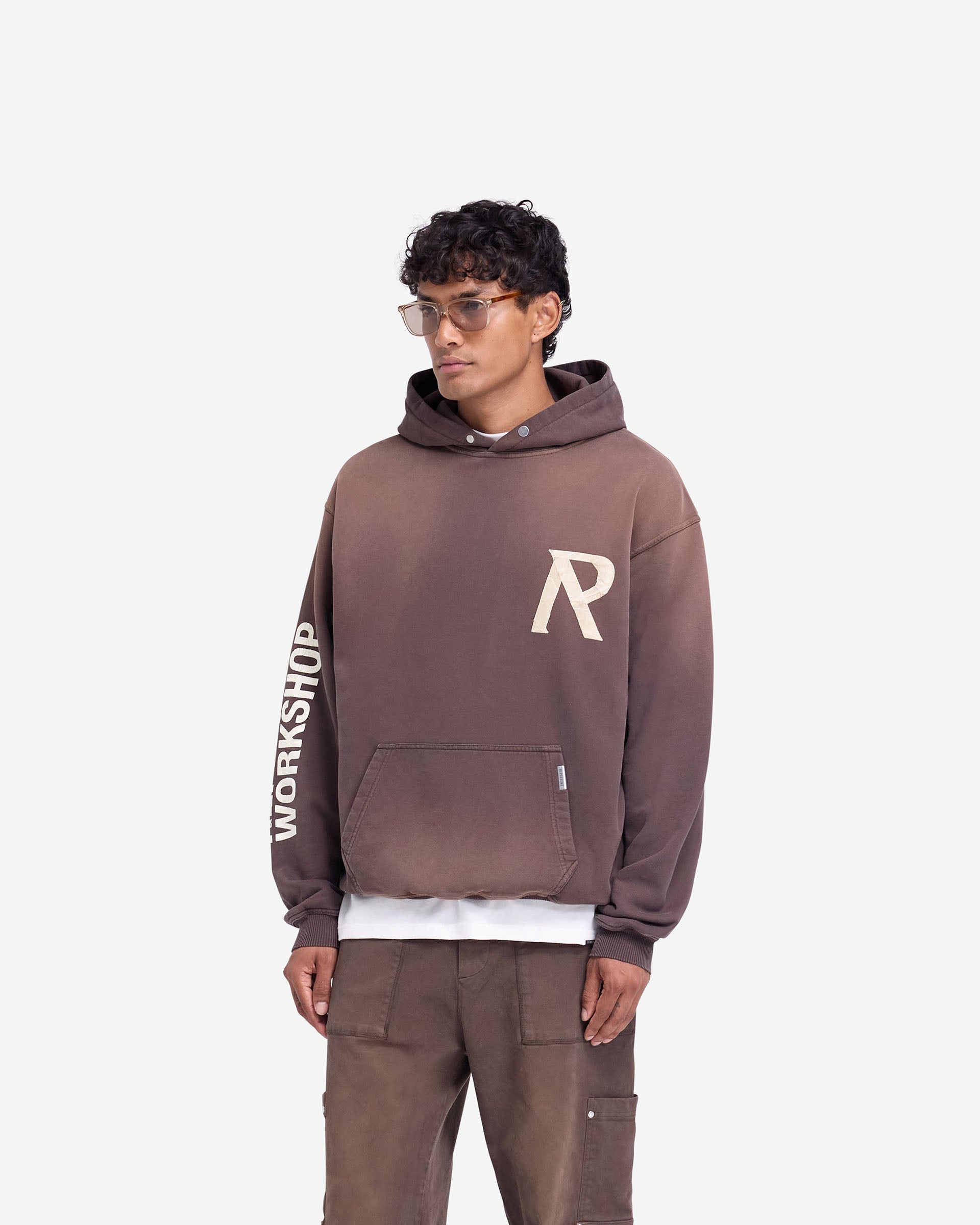 Man wearing a slightly oversized green hoodie on a plain white background | Masking Tape Initial Hoodie in Cedar | Heavy weight jersey hoodie with 3D masking tape effect | FW24 Hoodies | Represent Clo
