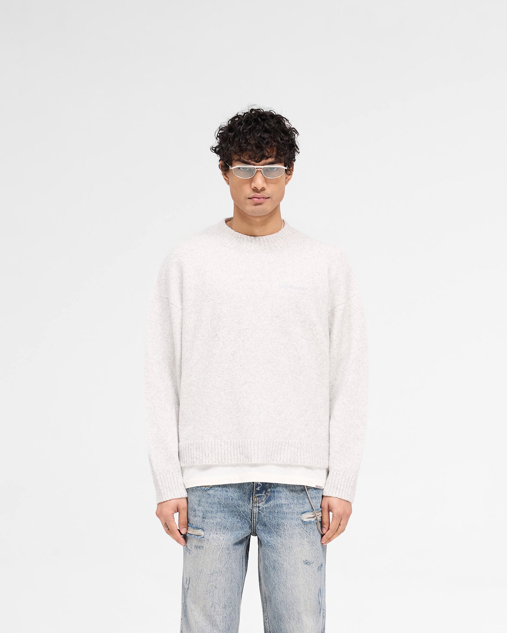Man wearing a grey jumper on a plain white background | Marled Knit Jumper in Ice Grey Marl | Knitwear with tonal script embroidery and ribbed detailing | SS25 Knitwear | Represent Clo