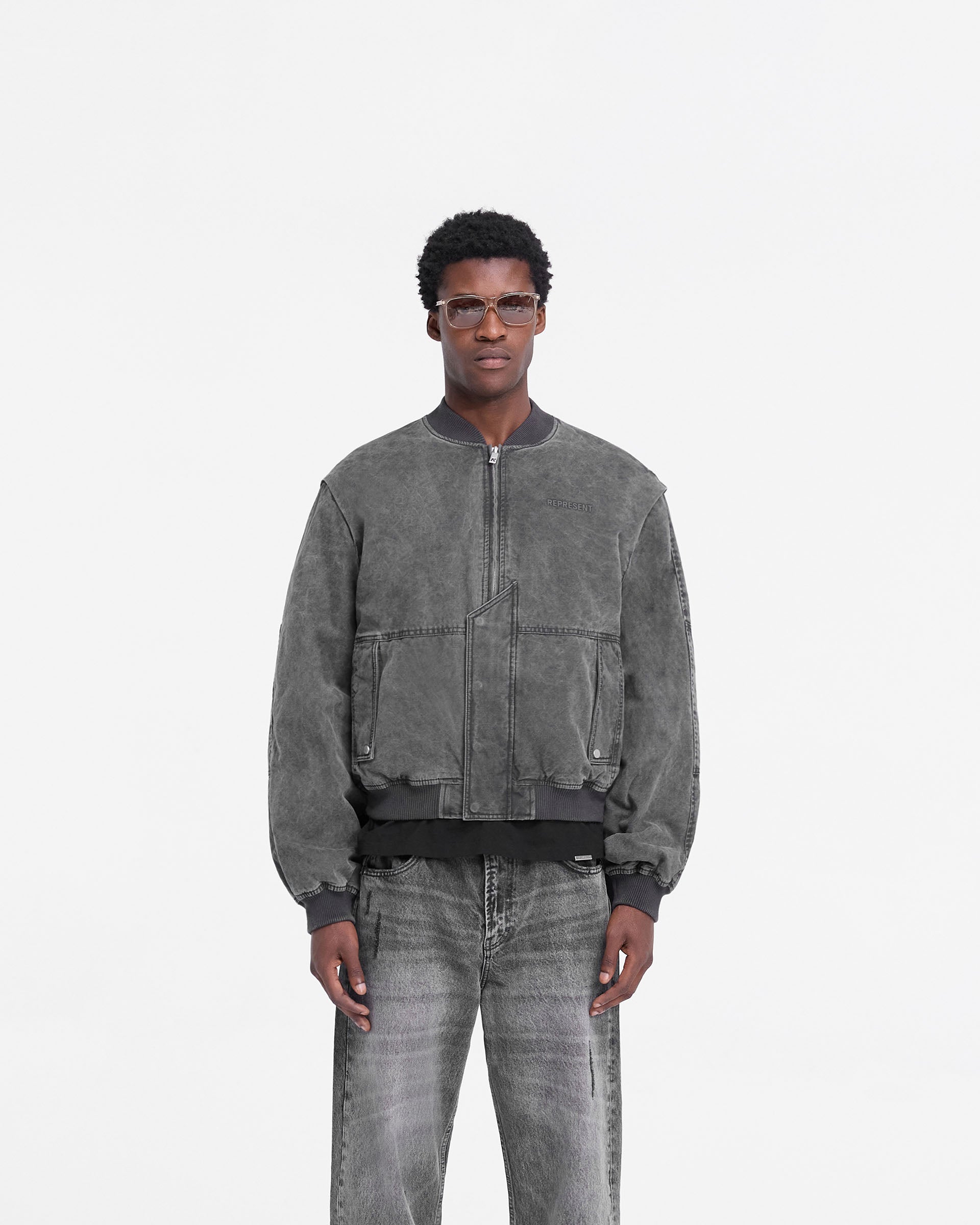 Man wearing a black bomber jacket on a plain white background | Inset Sleeve Bomber in Stained Black | Cotton bomber with asymmetric placket and zip guard | FW24 Outerwear | Represent Clo