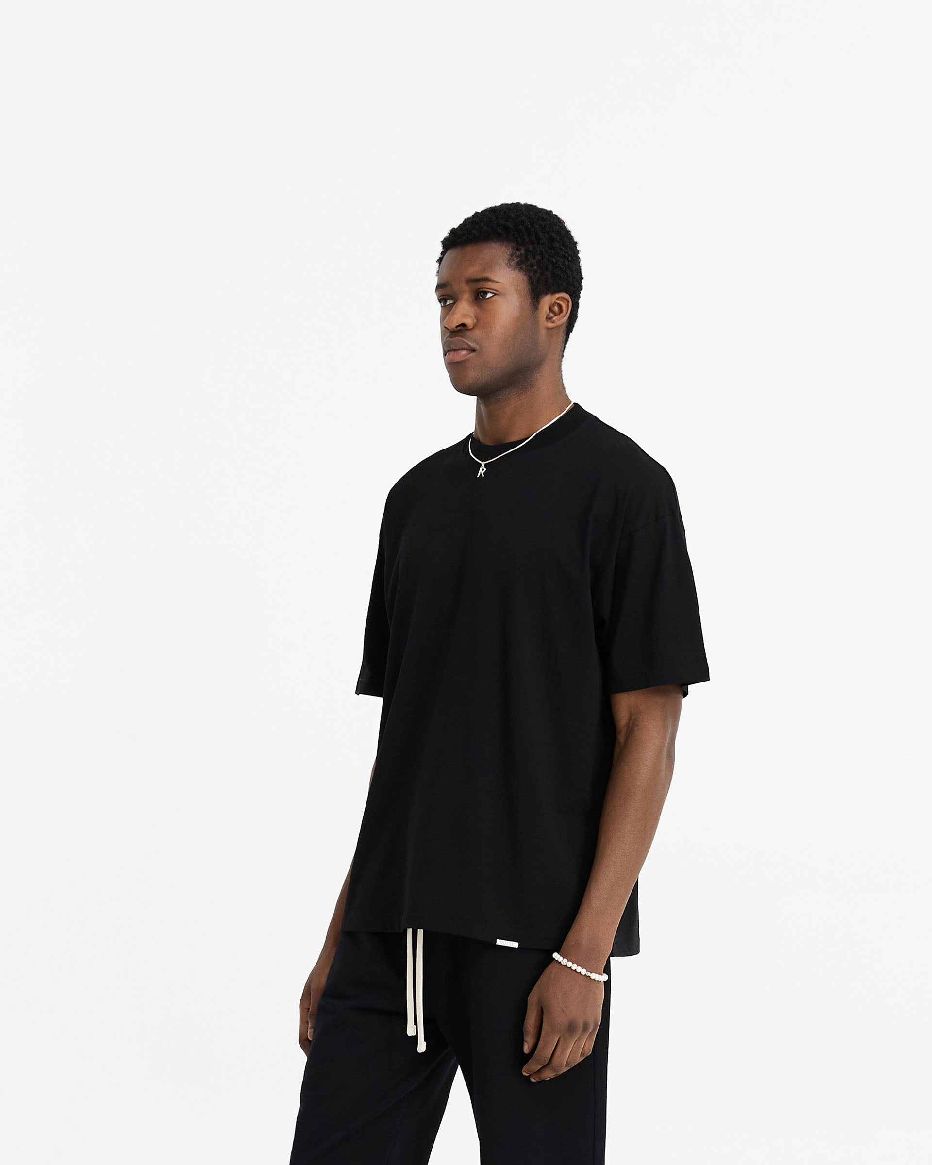 Back product image of a mens black t-shirt on a plain white background | Initial Oversized T-Shirt in Black | Oversized t-shirt with embroidered initial and metal bar logo | Initial T-Shirts | Represent Clo